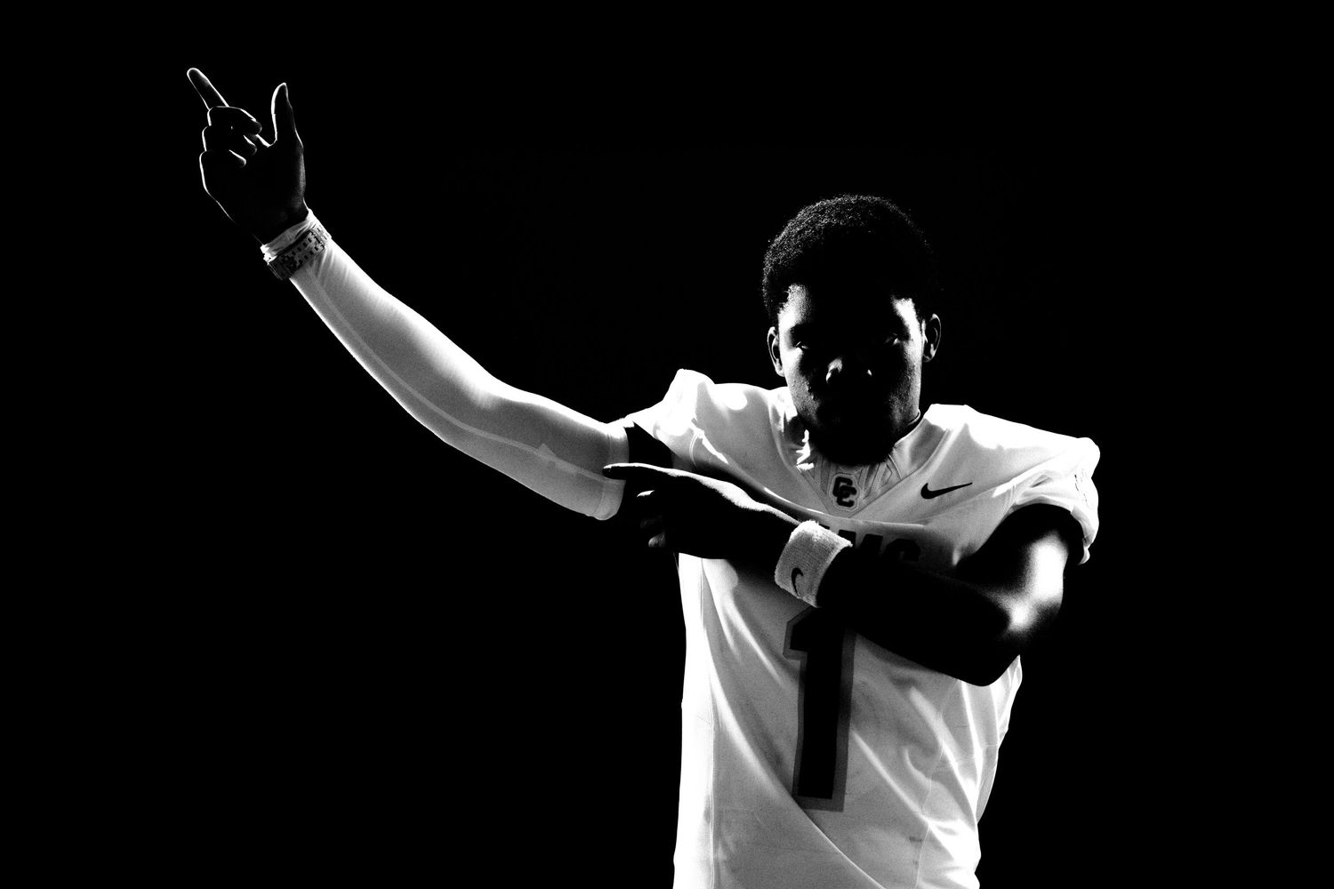Black and white photo of a football player in jersey number 1 raising hand under dramatic lighting.