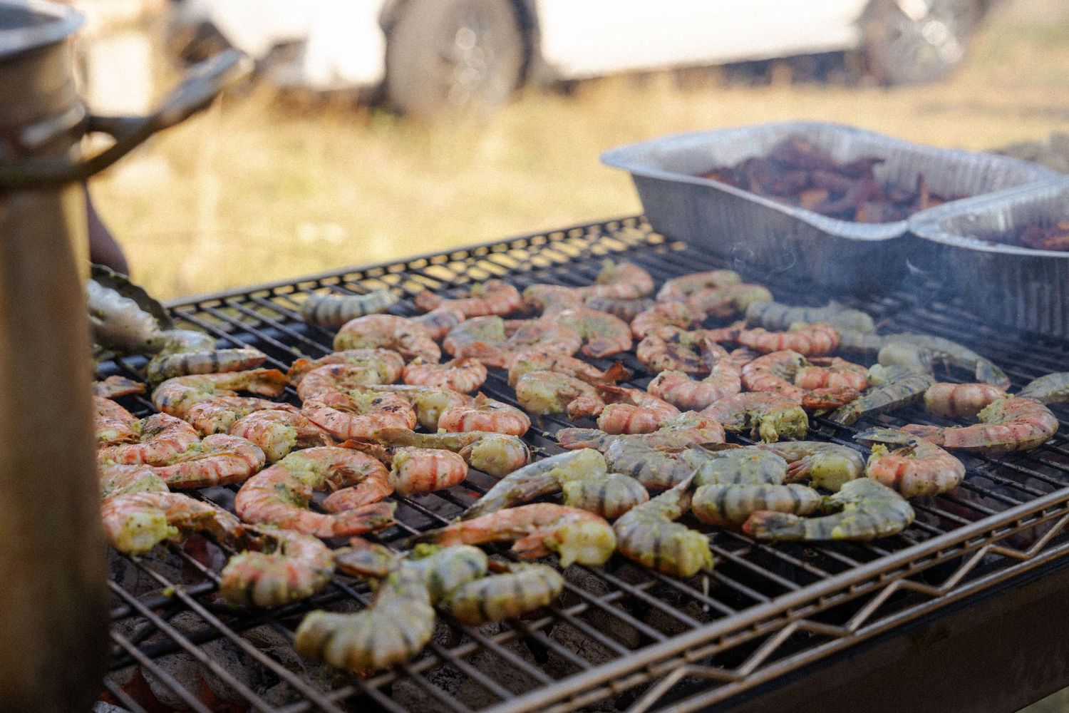 Fresh shrimp grilling on an outdoor barbecue grate with smoke rising, perfect for a seafood cookout.
