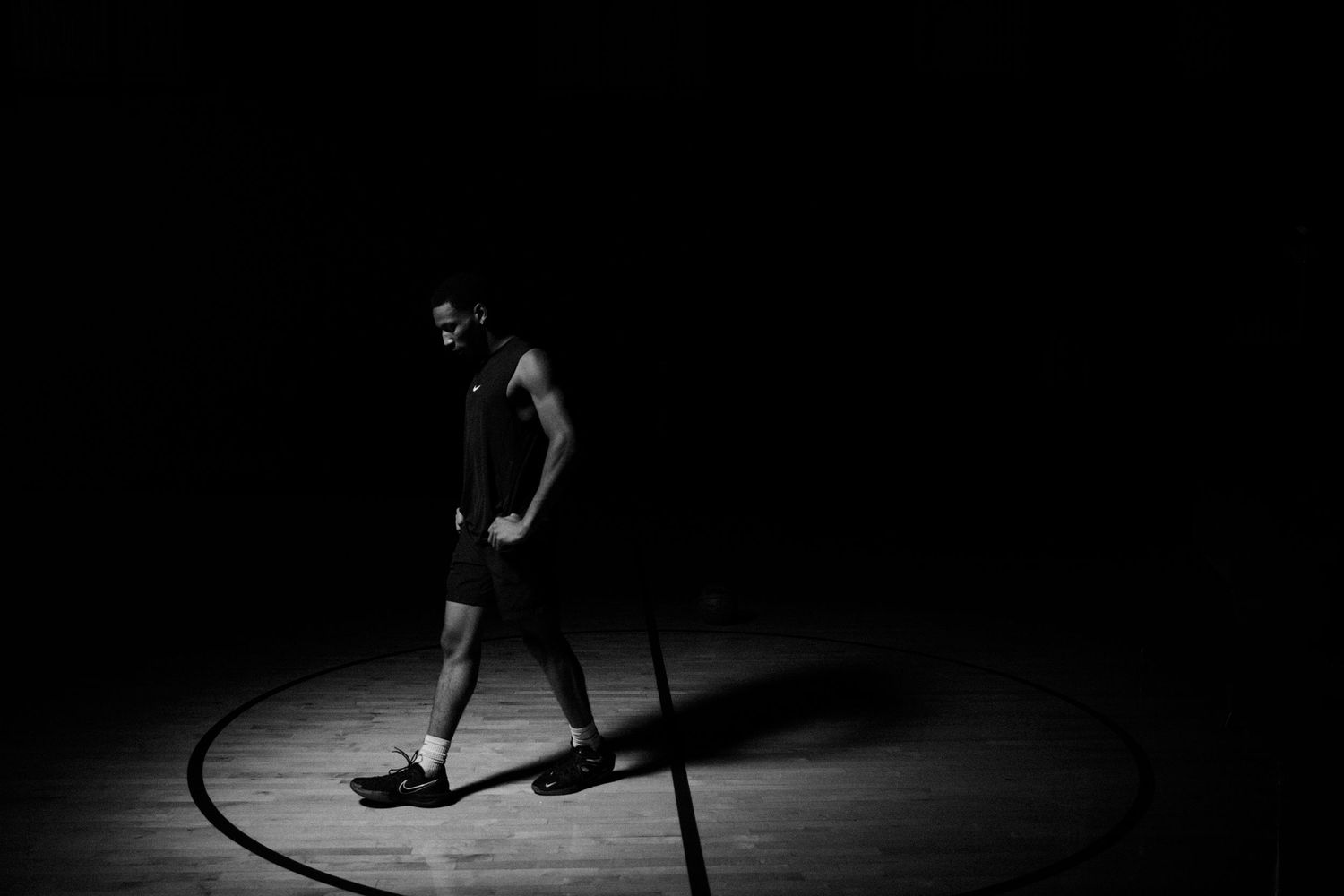 Lone basketball player standing in spotlight on empty court.