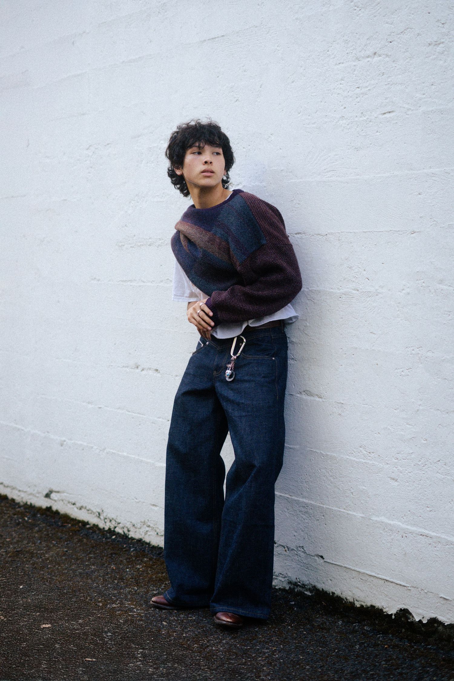 Figure in dark clothing posed against white wall near ground level.
