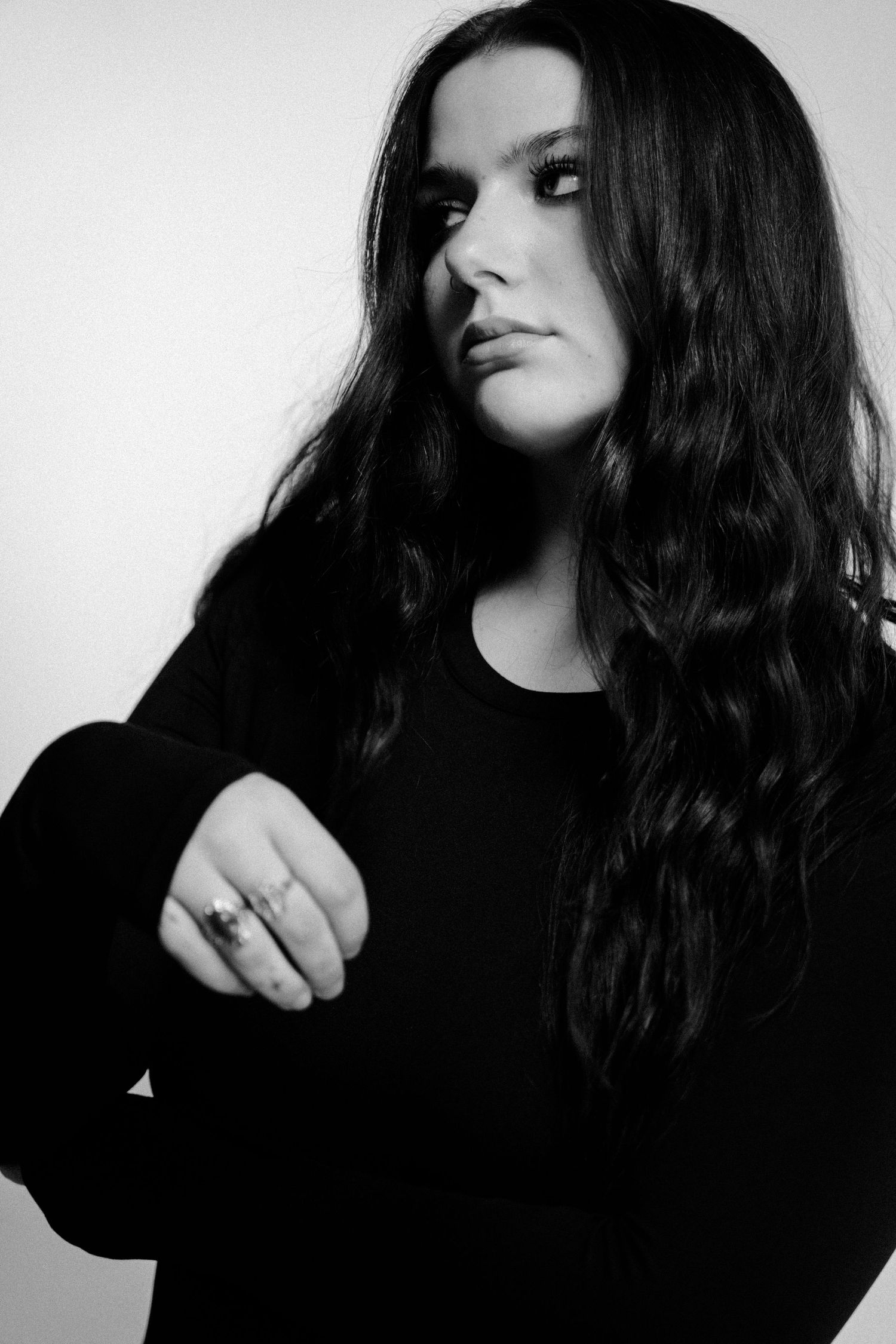 Black and white portrait of a young woman with long wavy dark hair wearing a black top and a ring.