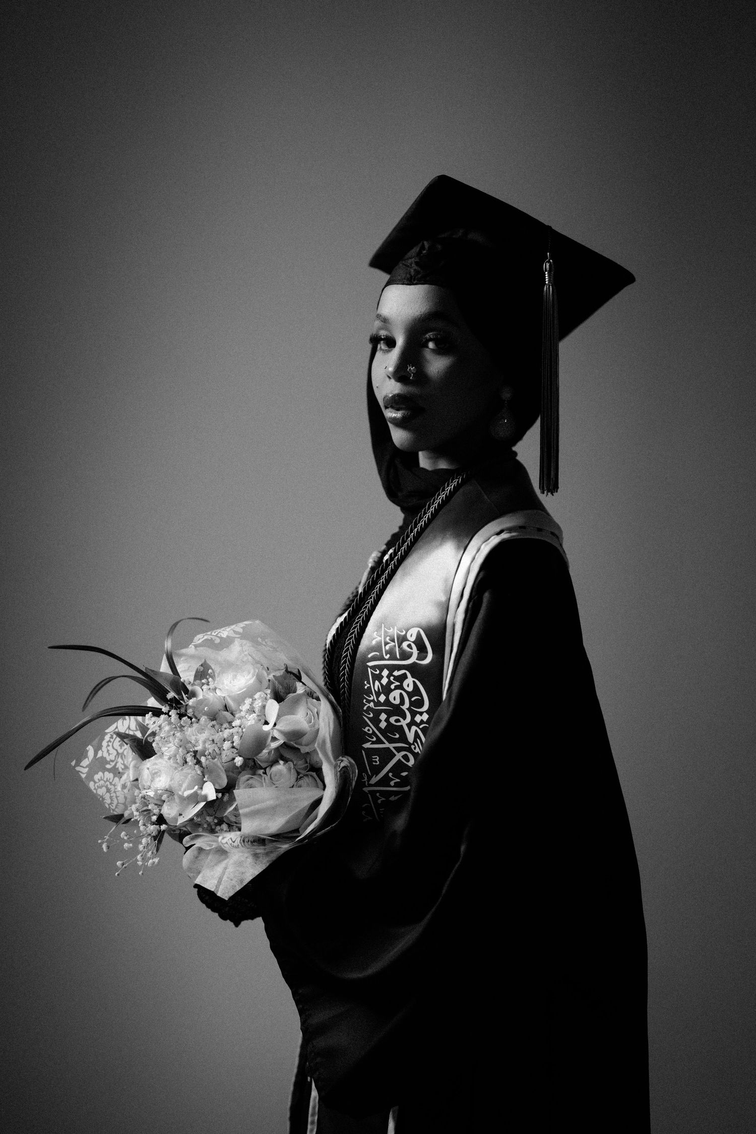 Artistic black and white graduation portrait featuring graduate holding flowers.