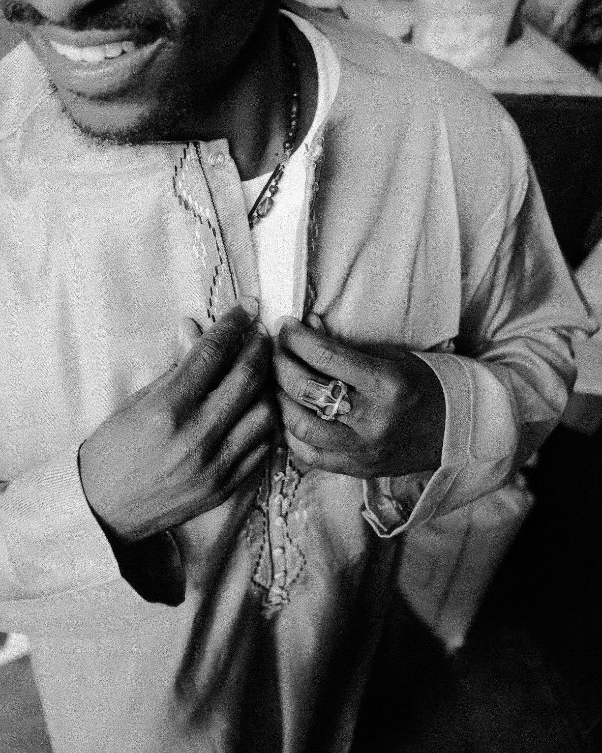 Person wearing light colored clothing and necklace in black and white portrait.
