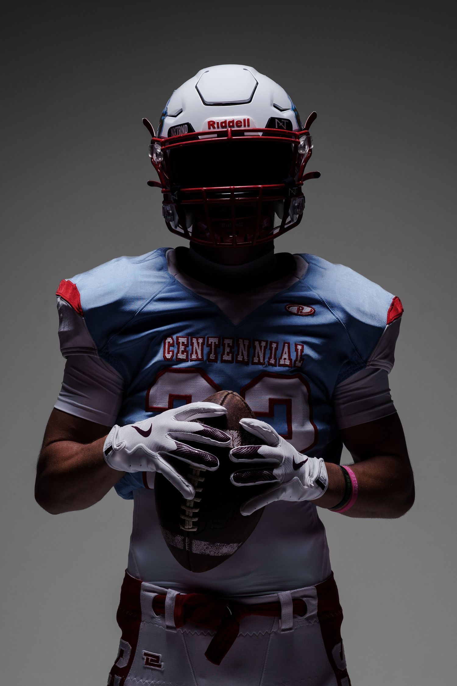 Football player in Centennial uniform holds ball in dramatic studio lighting.
