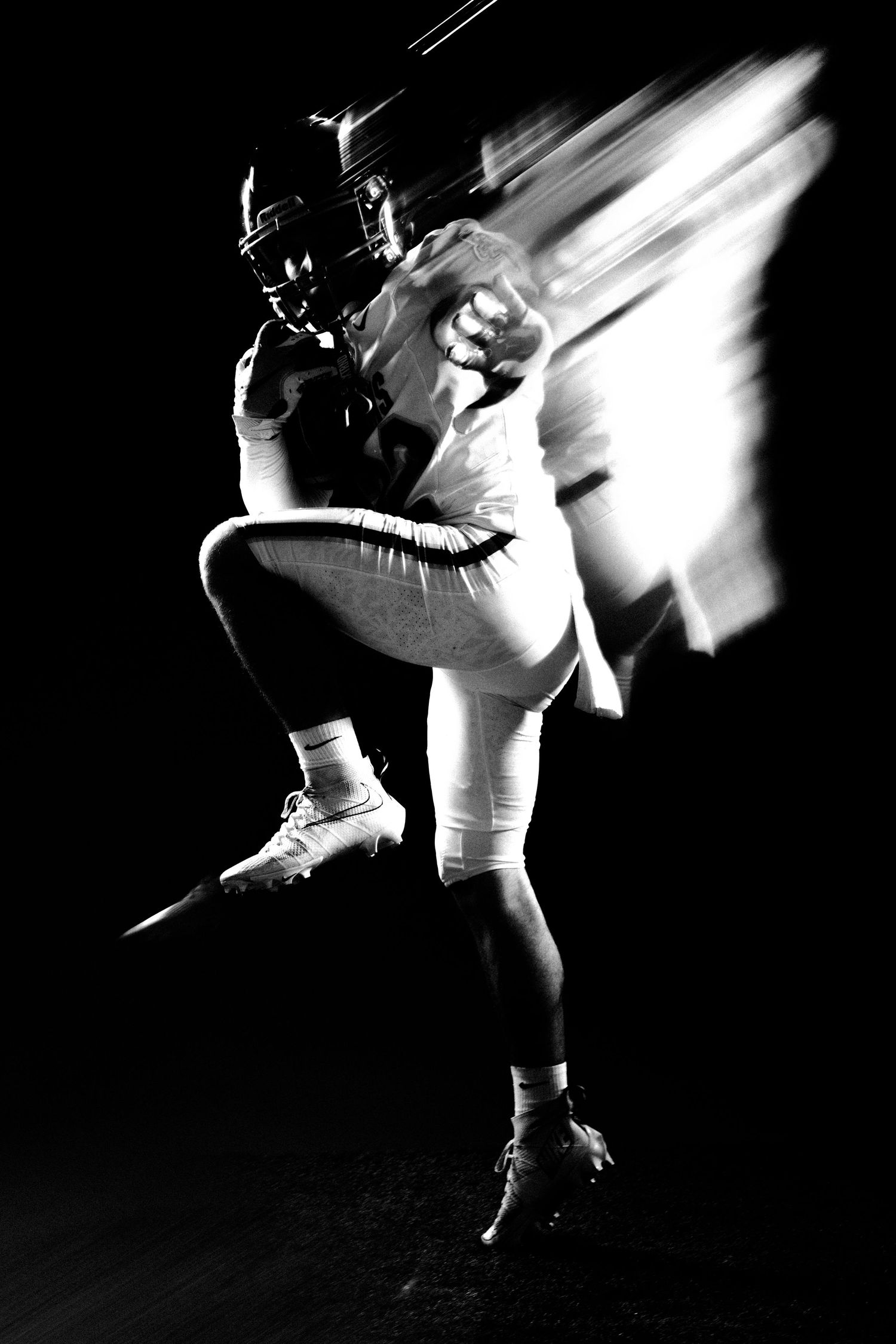 Black and white action shot of an American football player in motion, captured with dramatic blur effect against dark background.