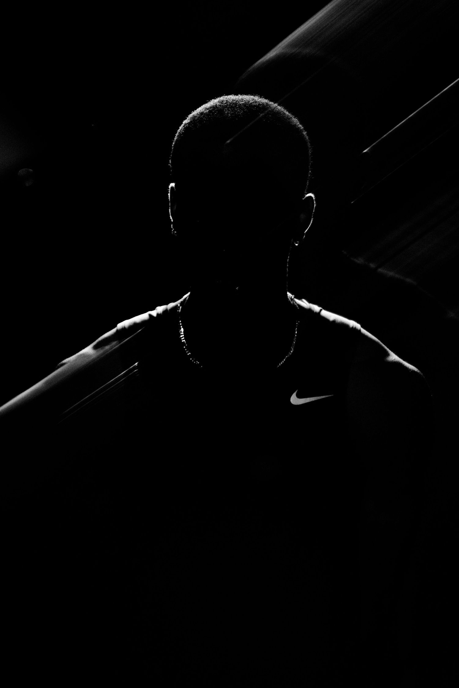 Silhouetted person wearing a Nike shirt dramatically lit in black and white against a dark background.