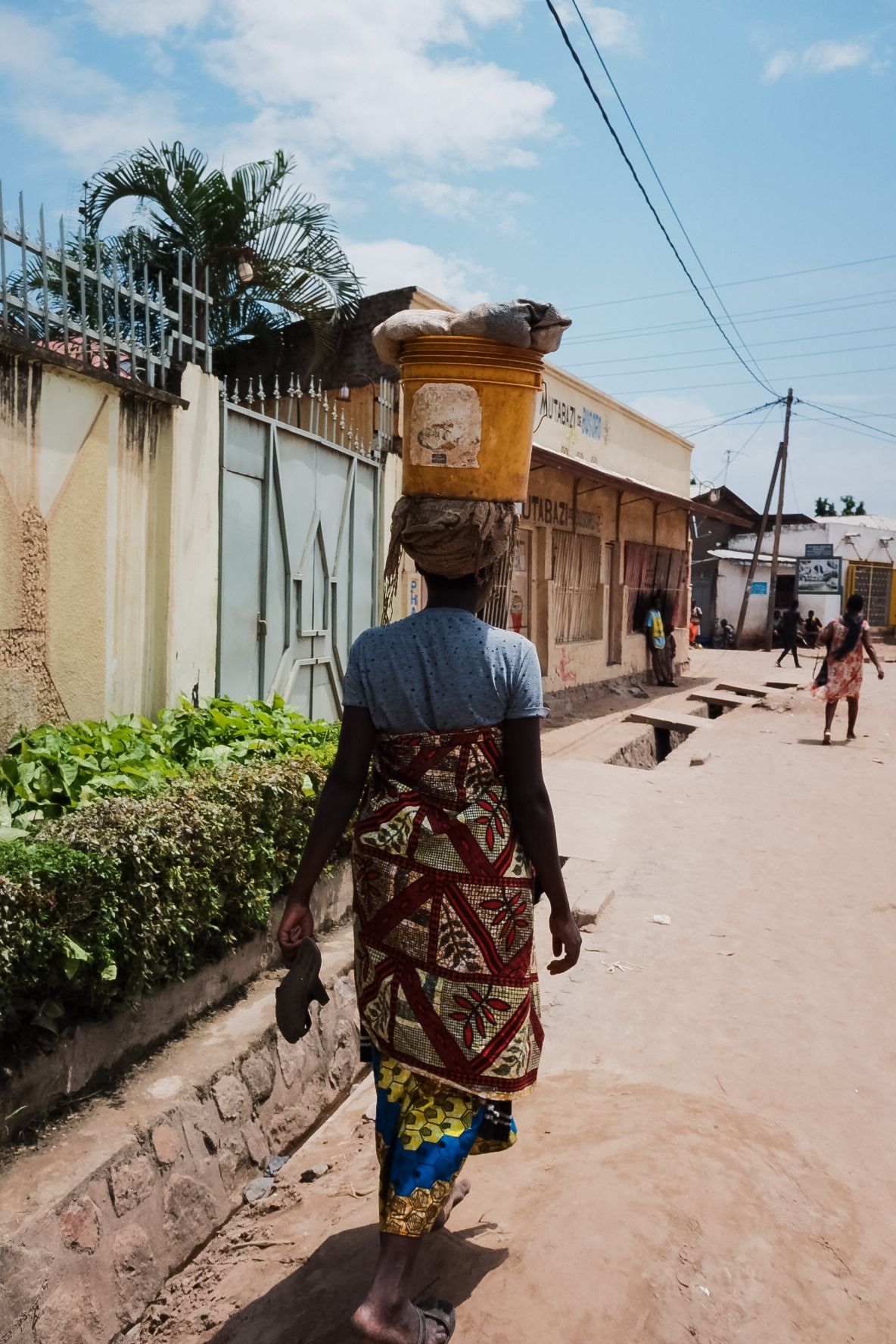 Person walking down a dusty street wearing traditional African clothing.