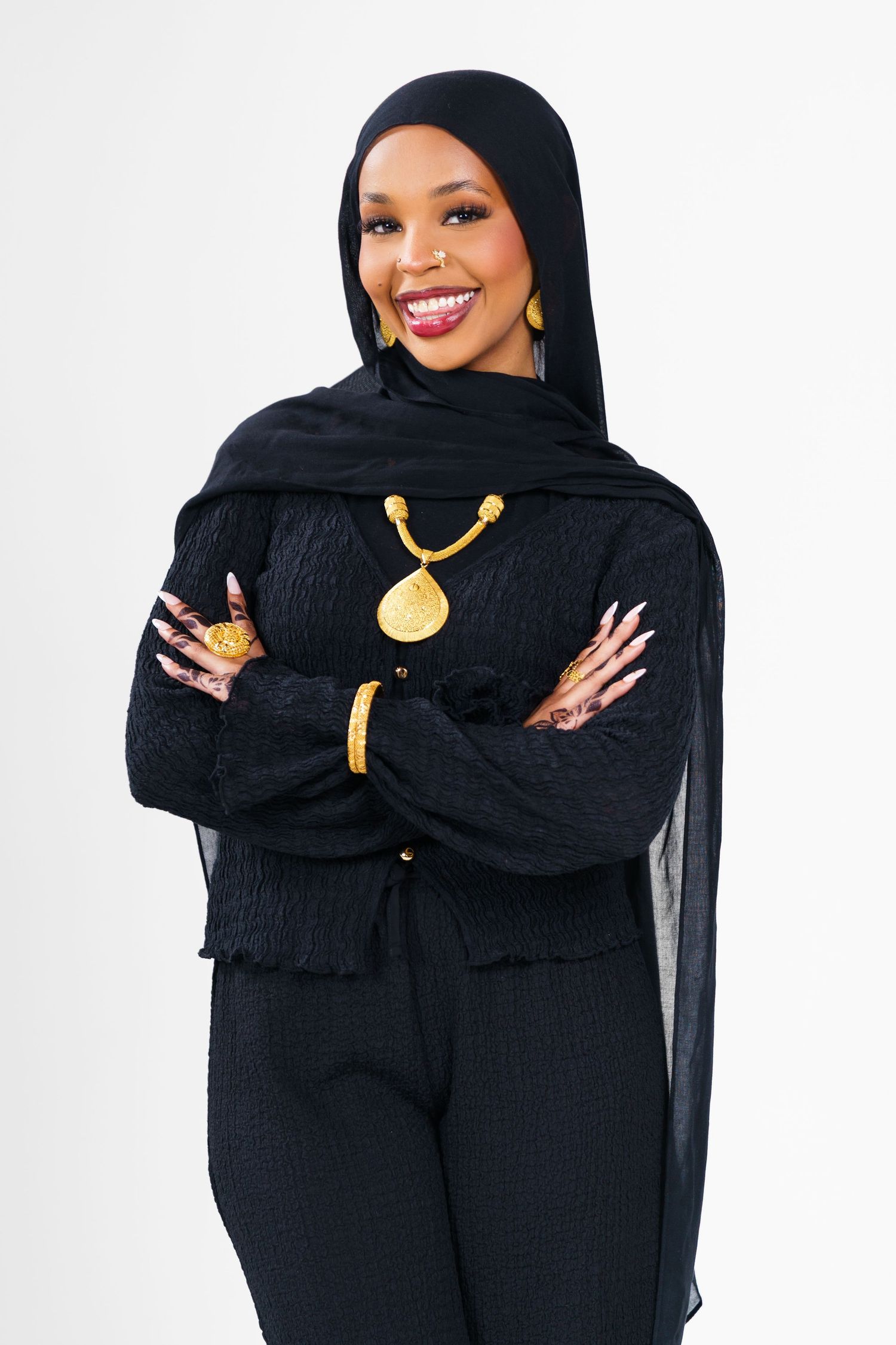 Graduate in black hijab and gold necklace poses confidently against white background.