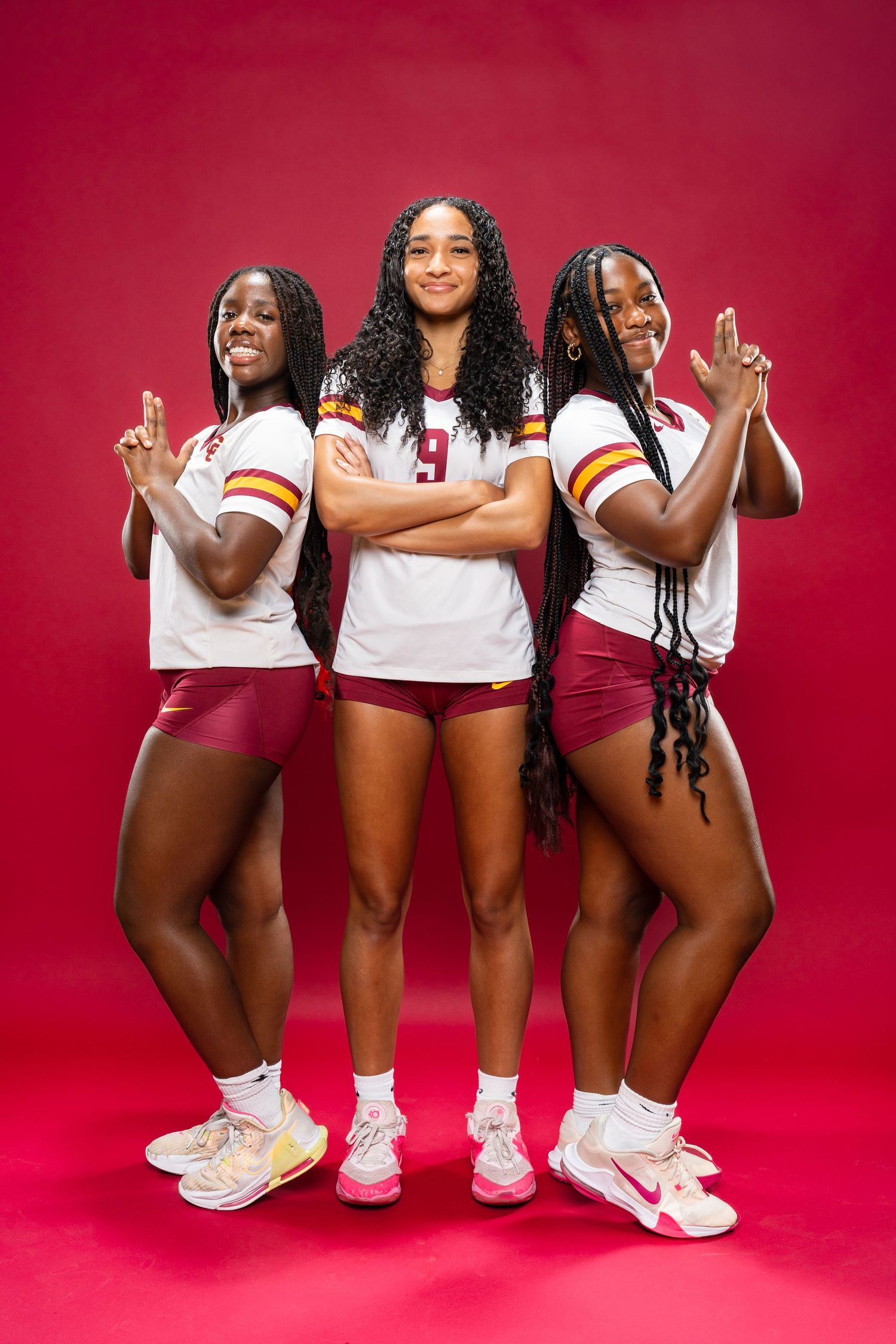 Athletes in white and maroon uniforms pose playfully against red studio background.