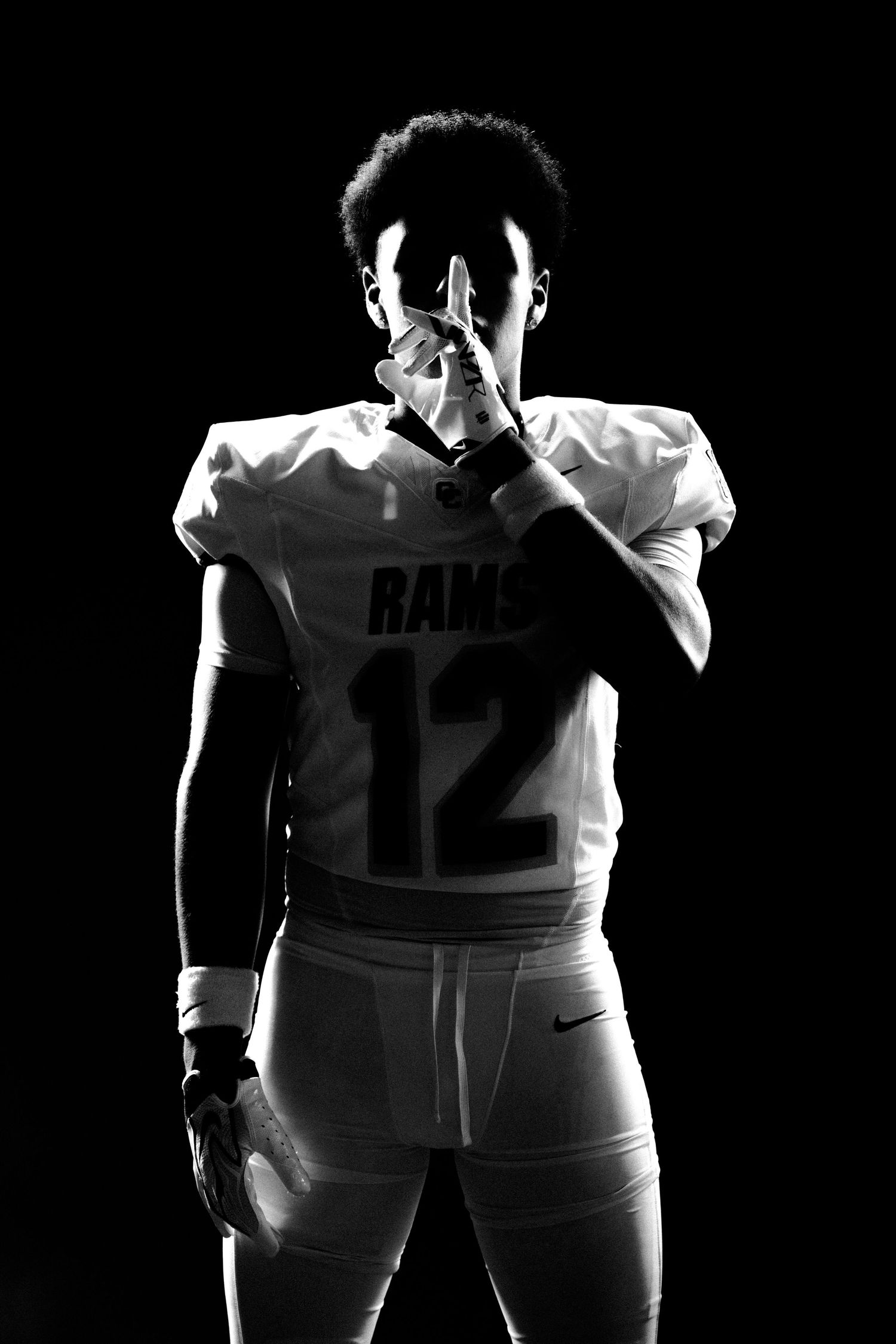 Black and white photo of a football player in Rams jersey number 12 posing dramatically against a dark background.
