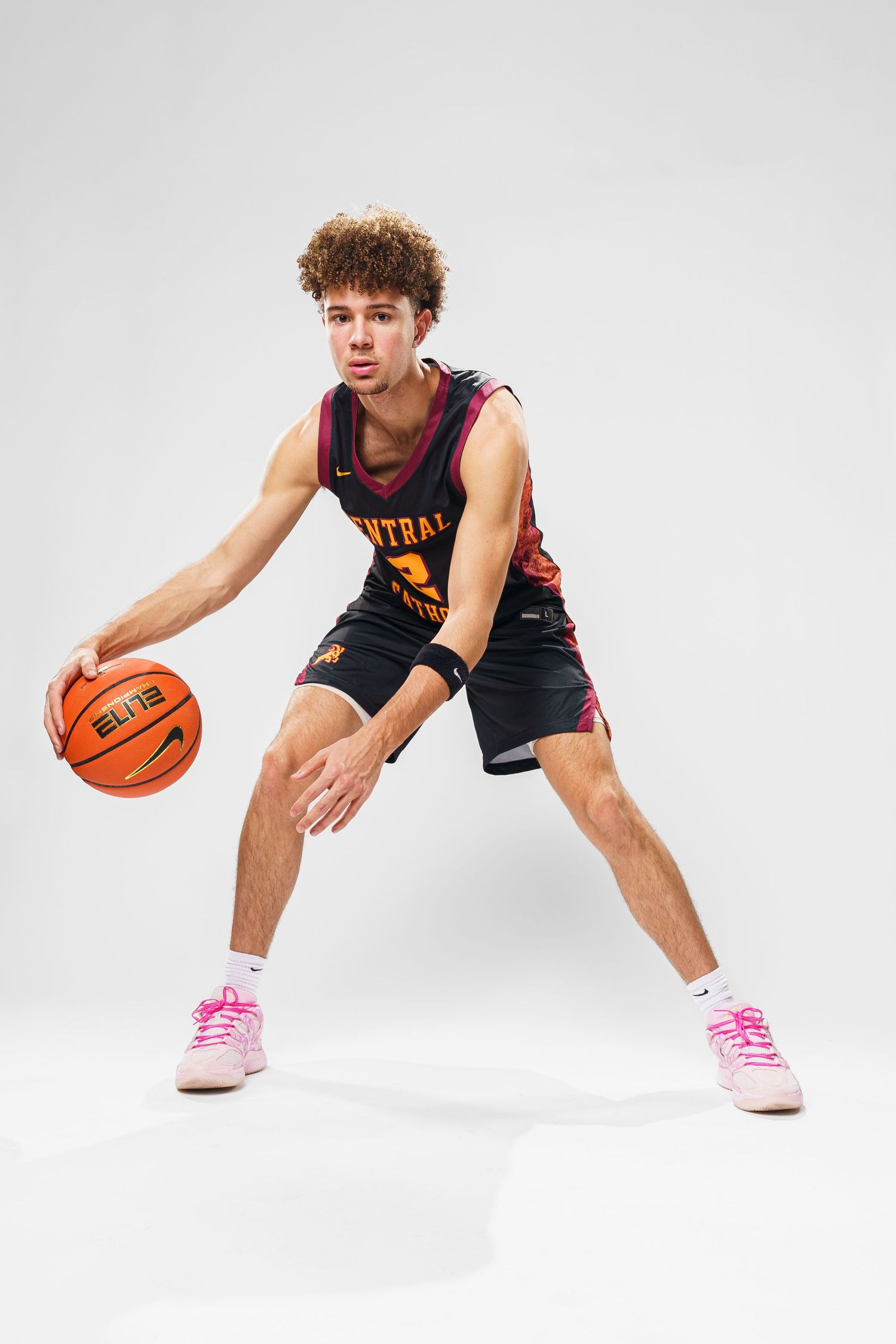 Basketball player in navy uniform demonstrates dribbling stance on white background.