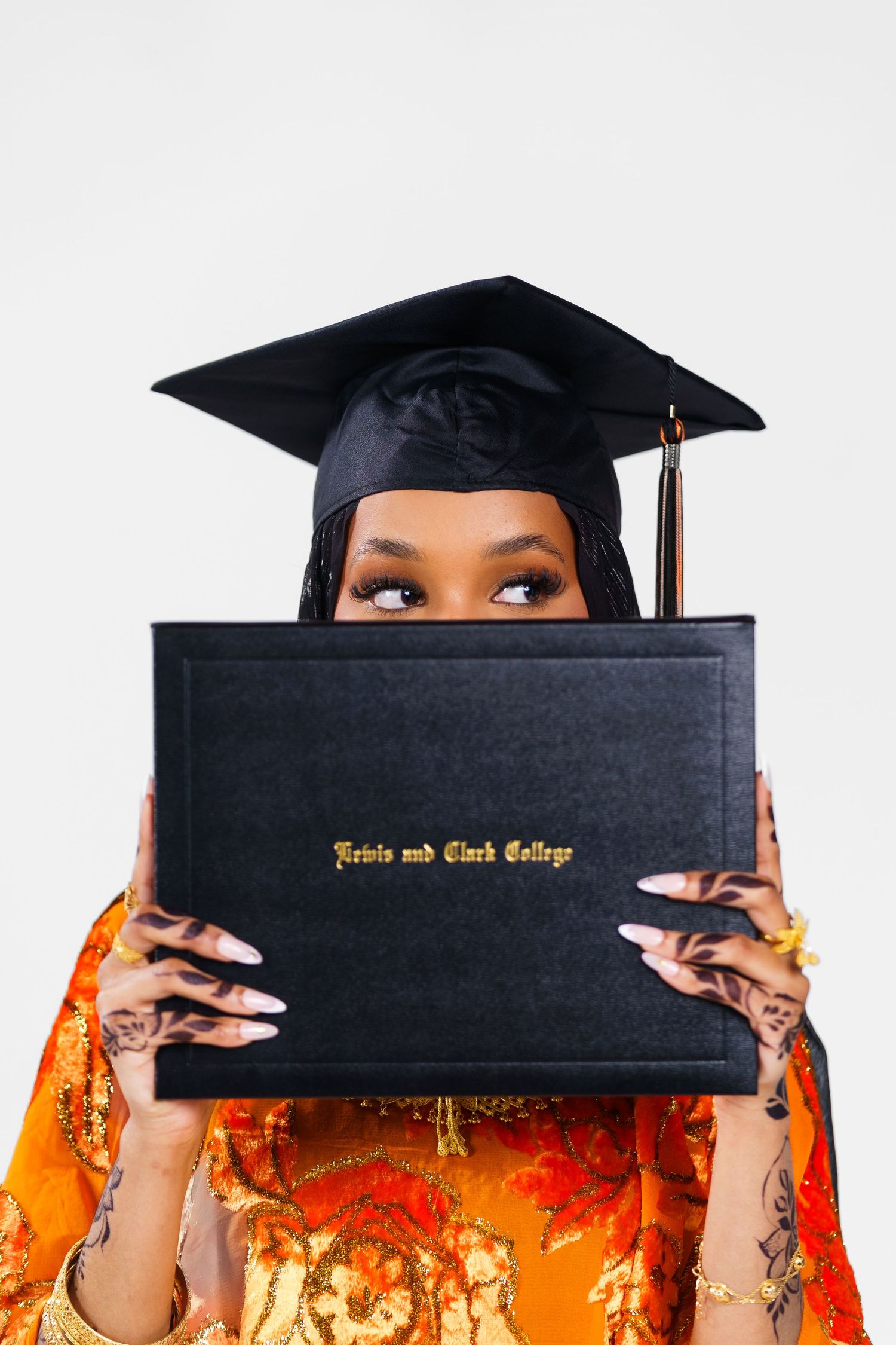 Graduate playfully poses with diploma holder wearing orange and black academic regalia.