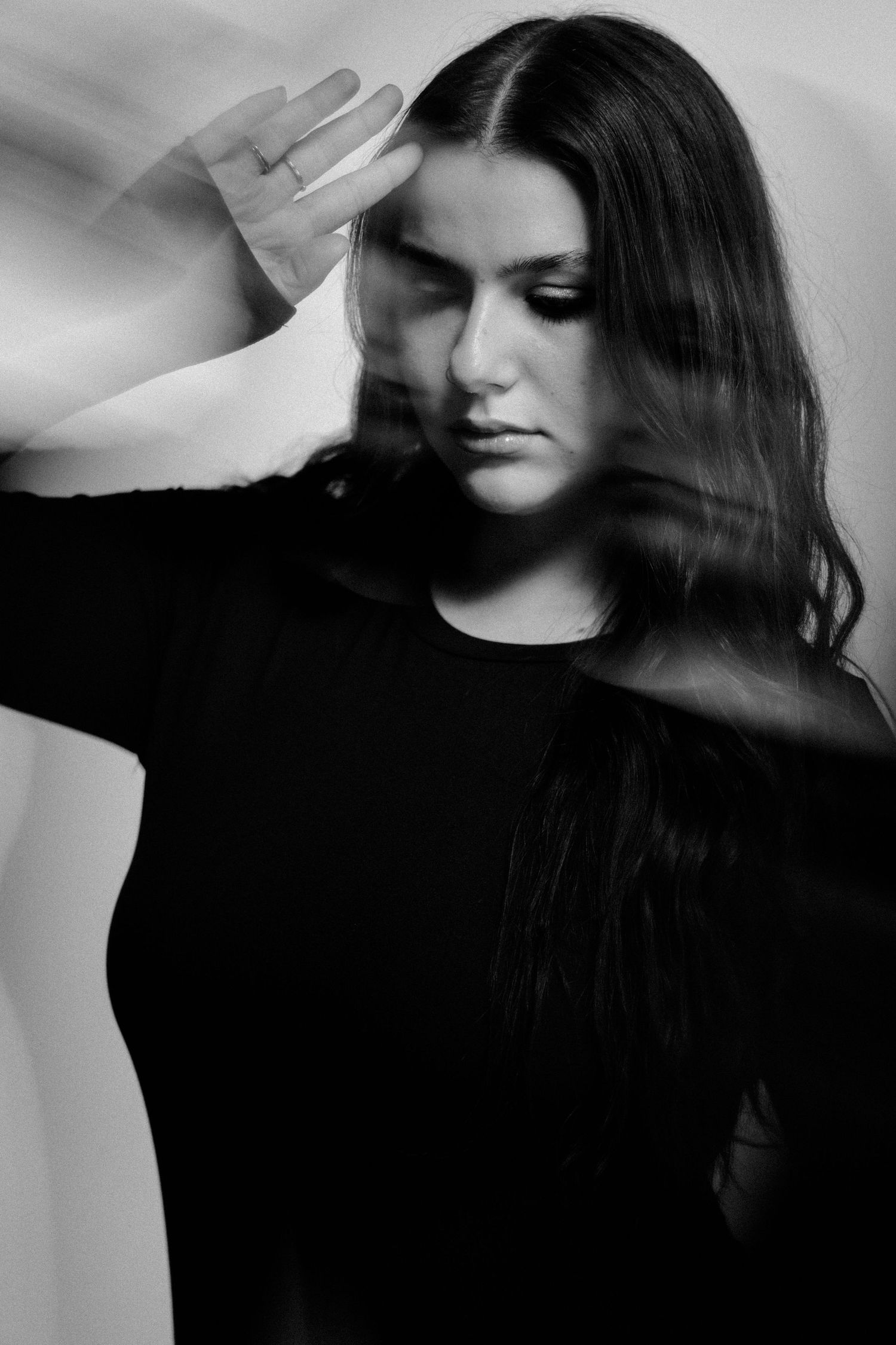Black and white portrait of a young woman in black top with motion blur effect, hand raised near face.