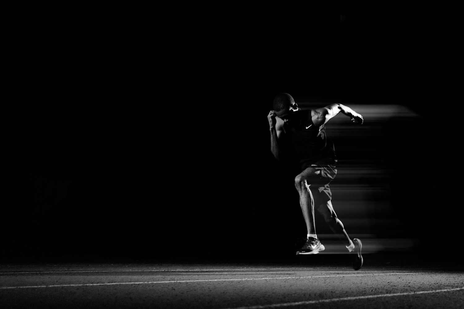 Black and white photo of a sprinter in motion blur, captured mid-stride against a dark background.