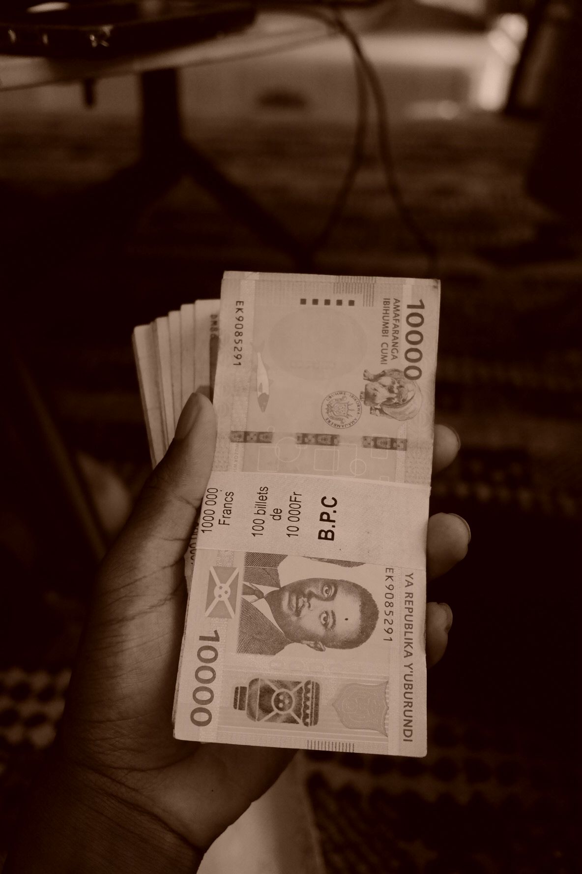 Close-up of West African currency notes being held in dim lighting.