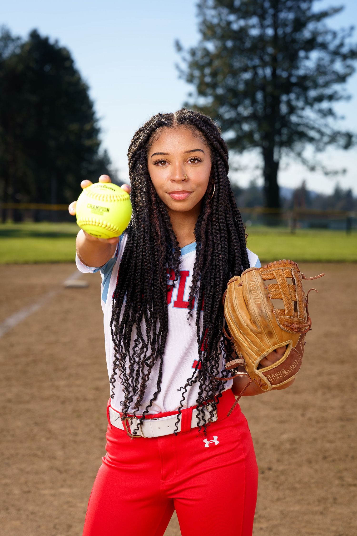 A softball player in red pants and white top demonstrates different pitching and fielding poses on a dirt field.