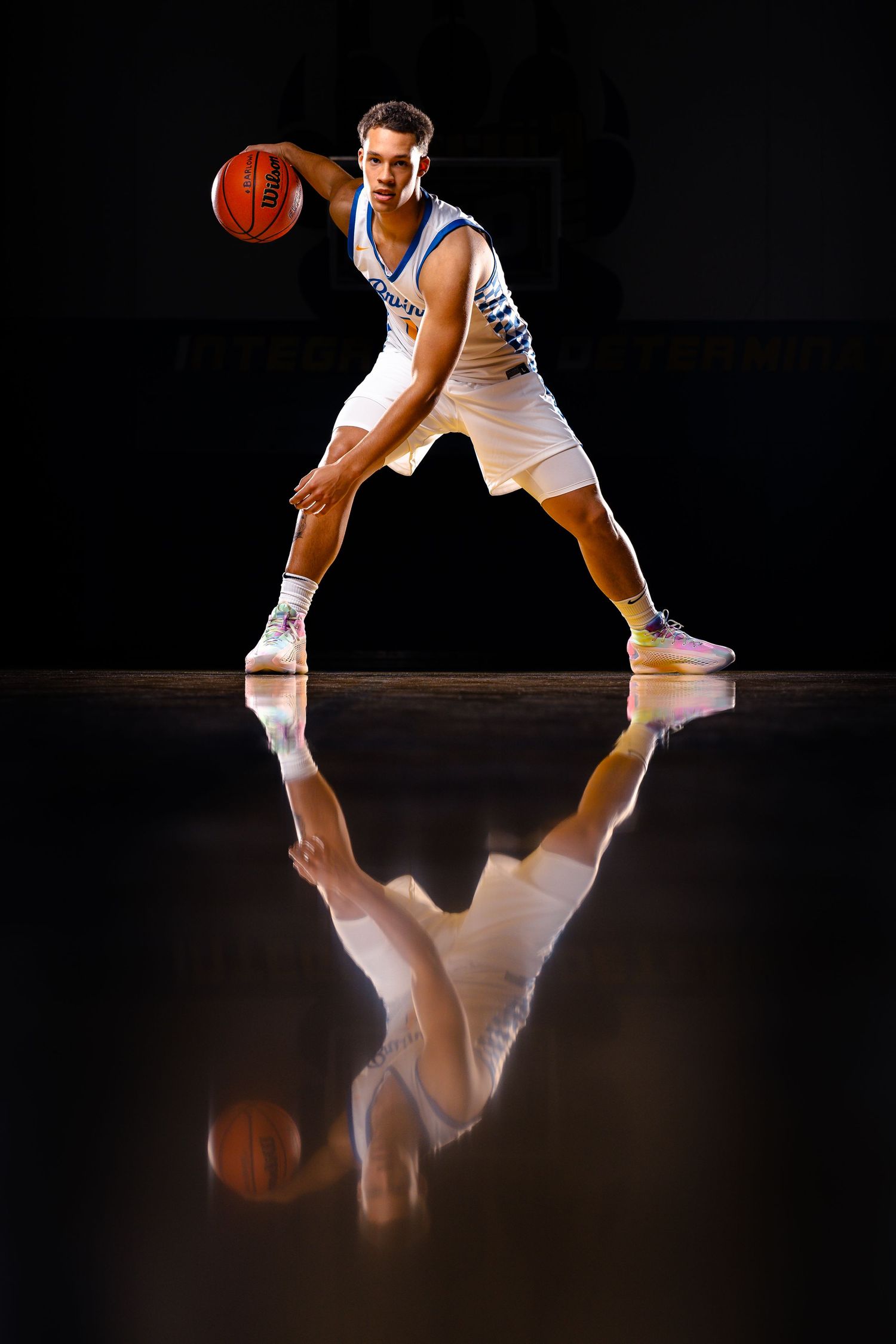 Basketball player in white uniform dribbles ball on reflective court surface.