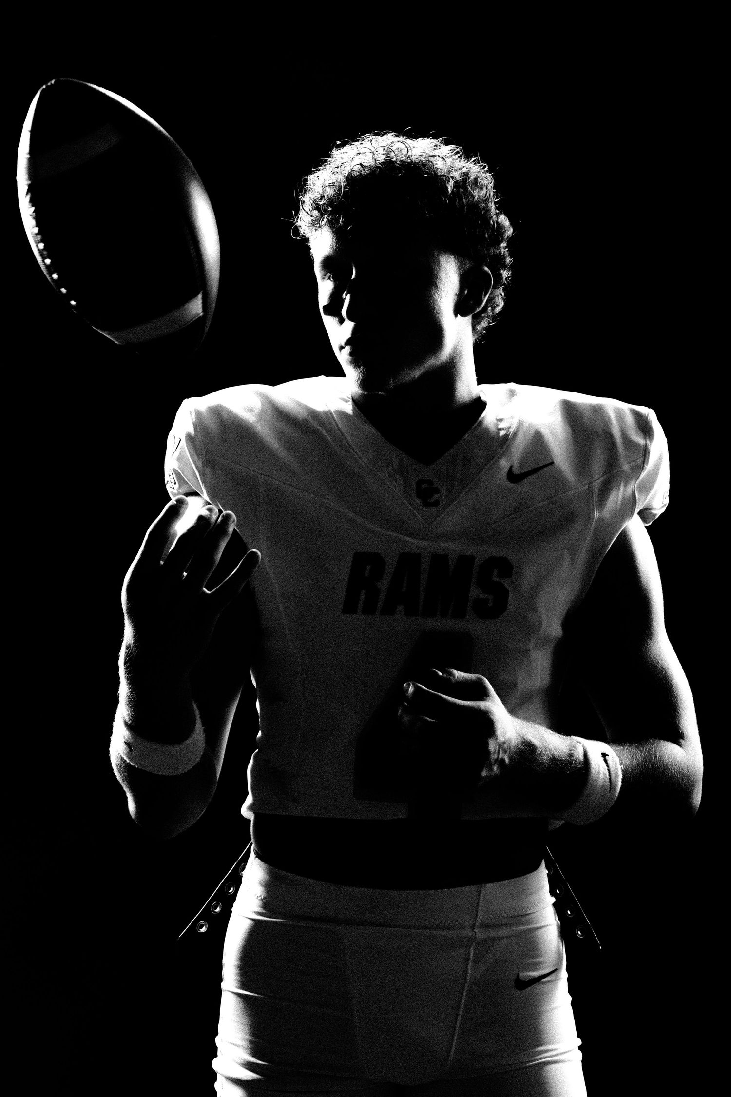 Black and white silhouette of a Rams football player tossing a football, dramatic studio lighting.