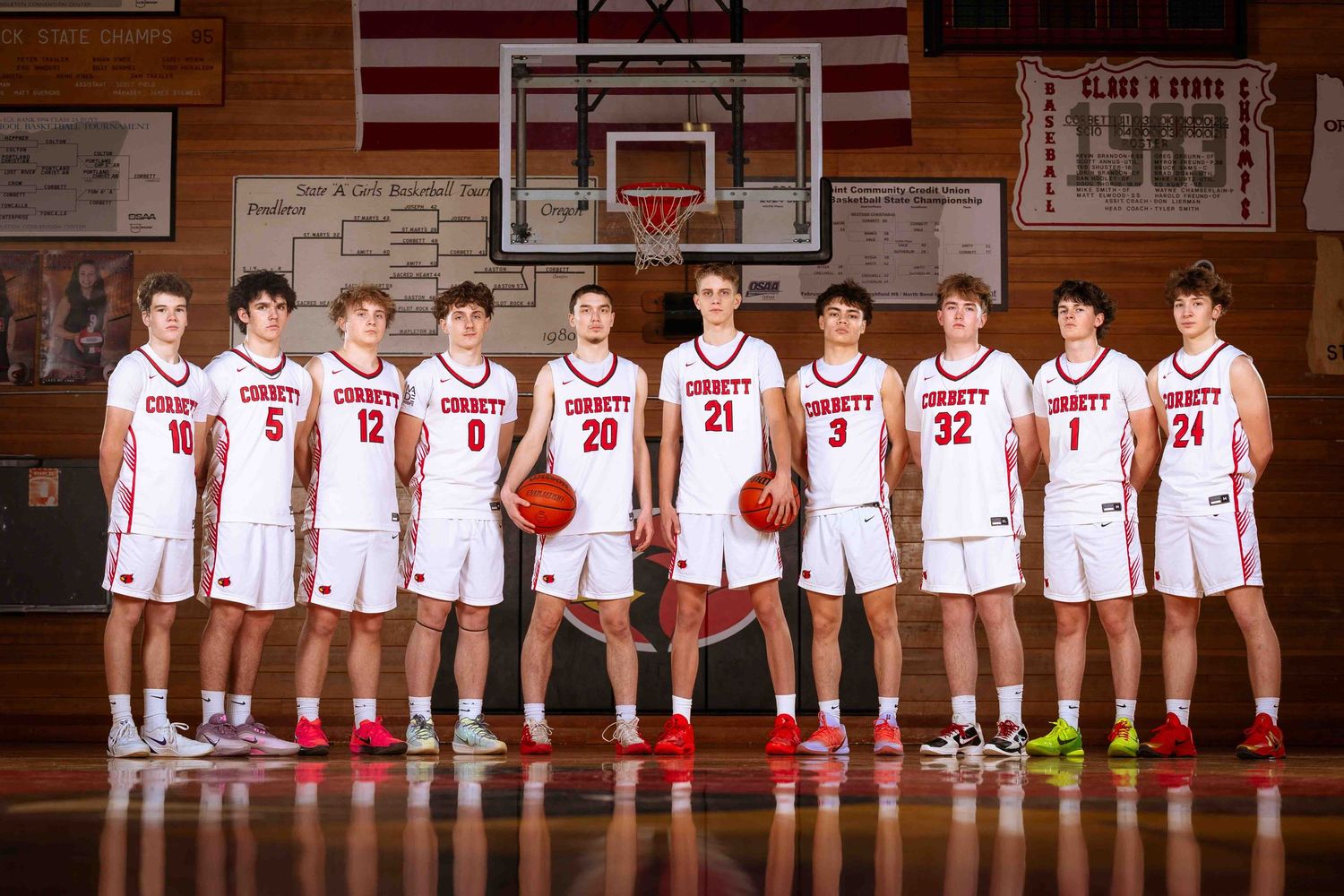 High school basketball team poses in white and red uniforms on a wooden court for their official group photo.