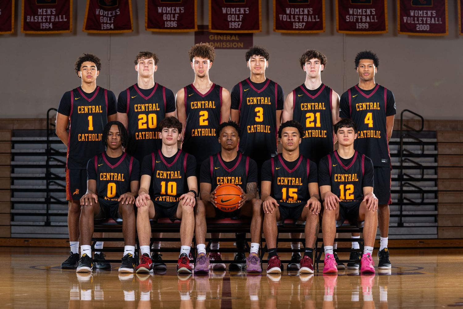 High school basketball team poses for group photo in black uniforms on court.