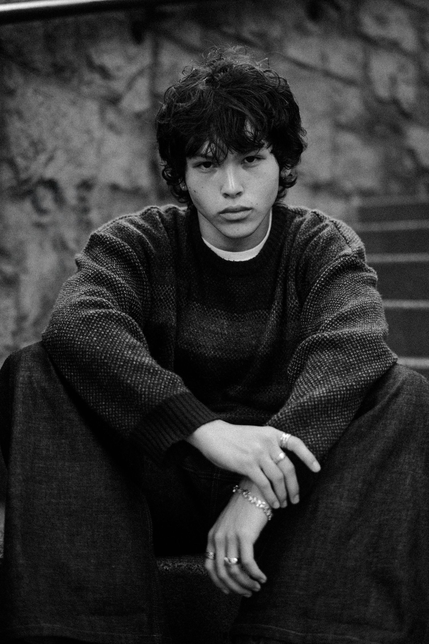 Black and white portrait of figure in sweater sitting on steps.