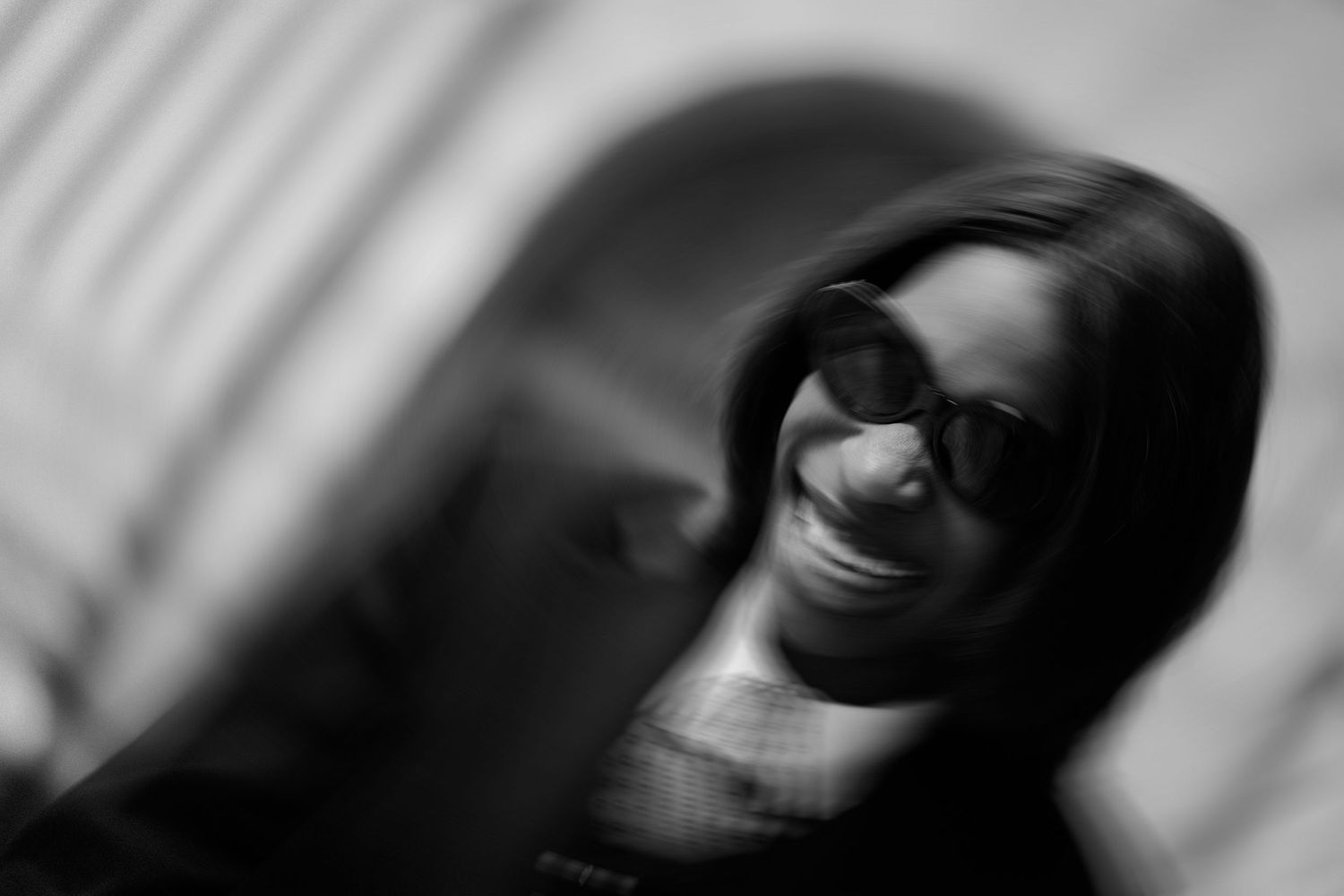 Black and white portrait of a smiling woman wearing round glasses, with artistic blur effect.