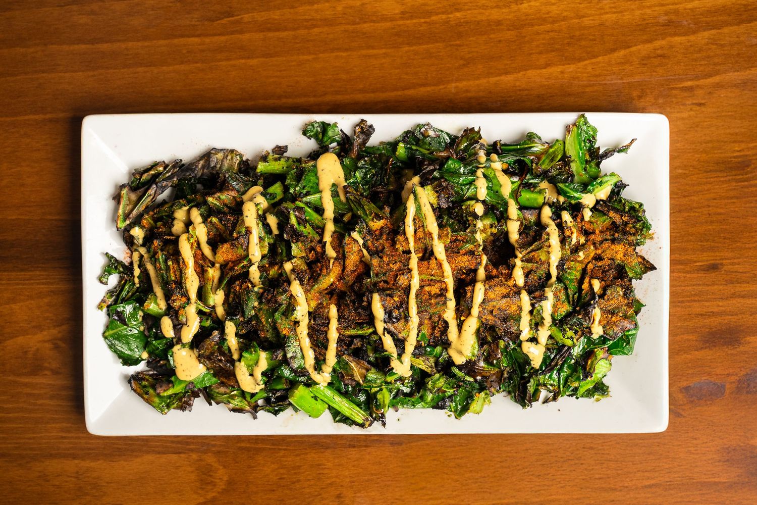 Roasted kale salad topped with golden mustard drizzle on a white rectangular plate, served on a wooden table.