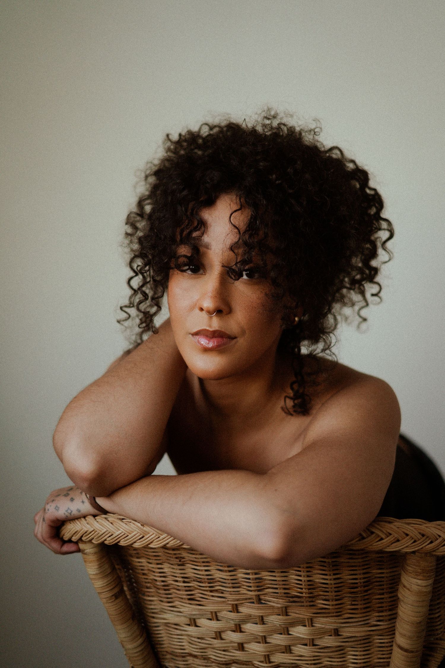 Artistic portrait series featuring curly hair and a wicker chair against a neutral background.