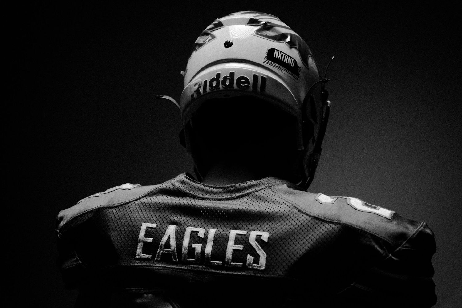 Silhouetted football players in Eagles uniforms against dark background.
