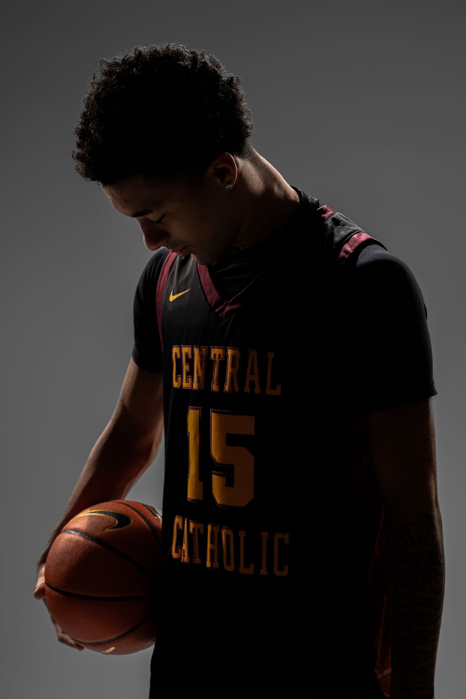 Basketball player in Central Catholic jersey number 15 poses with ball in moody lighting.