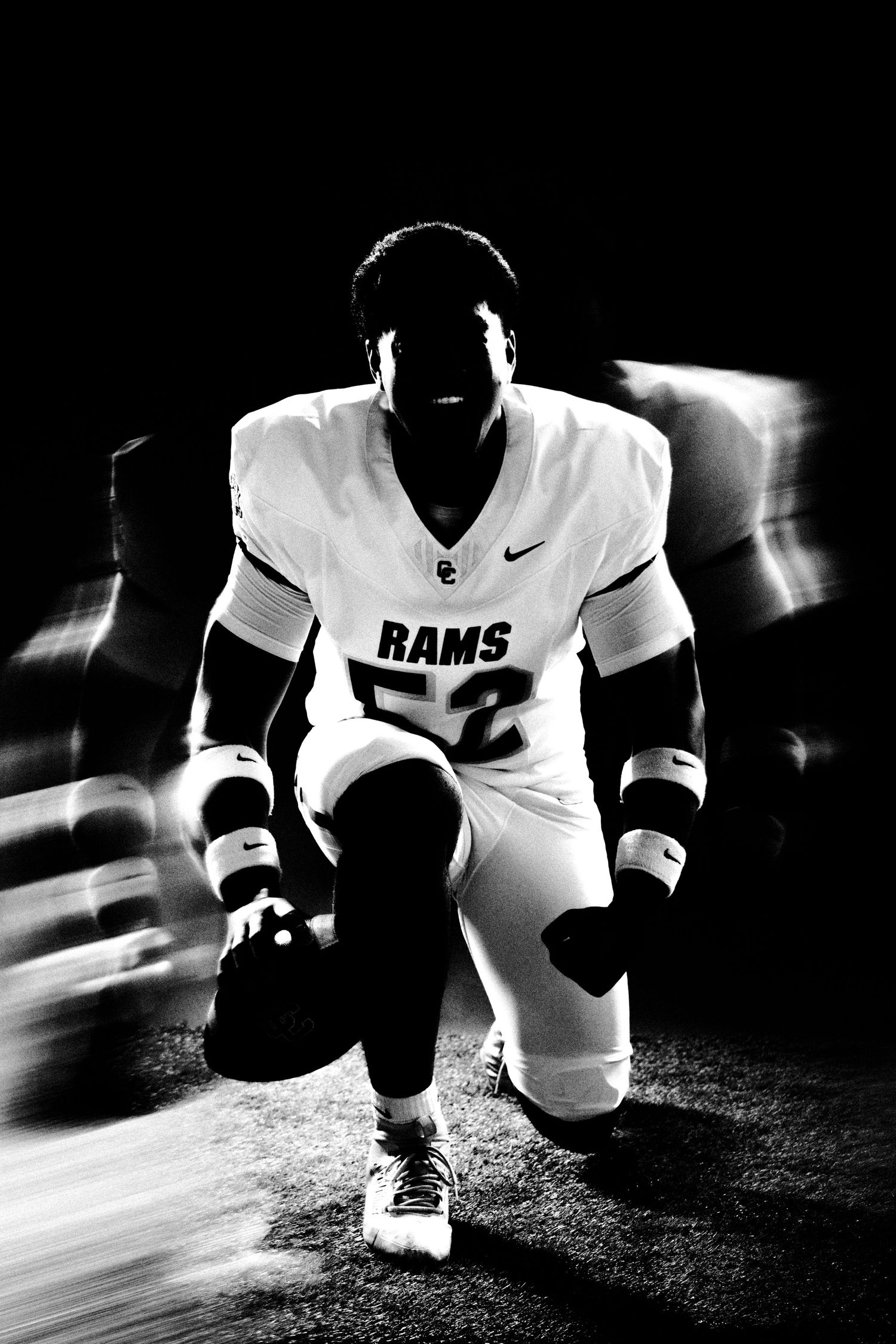 Black and white photo of Rams football player #52 kneeling dramatically with light streaks in dark stadium.