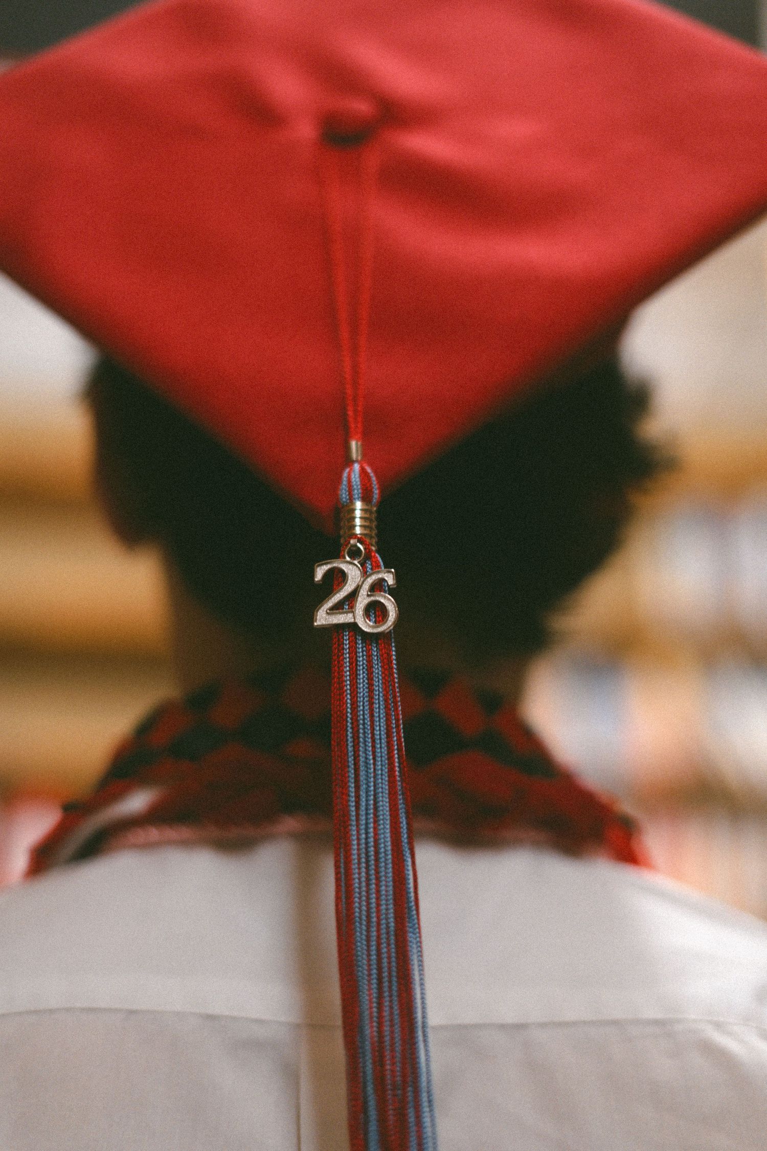 Close-up of a red graduation cap tassel with a silver '26' charm, worn by a graduate in a white gown.