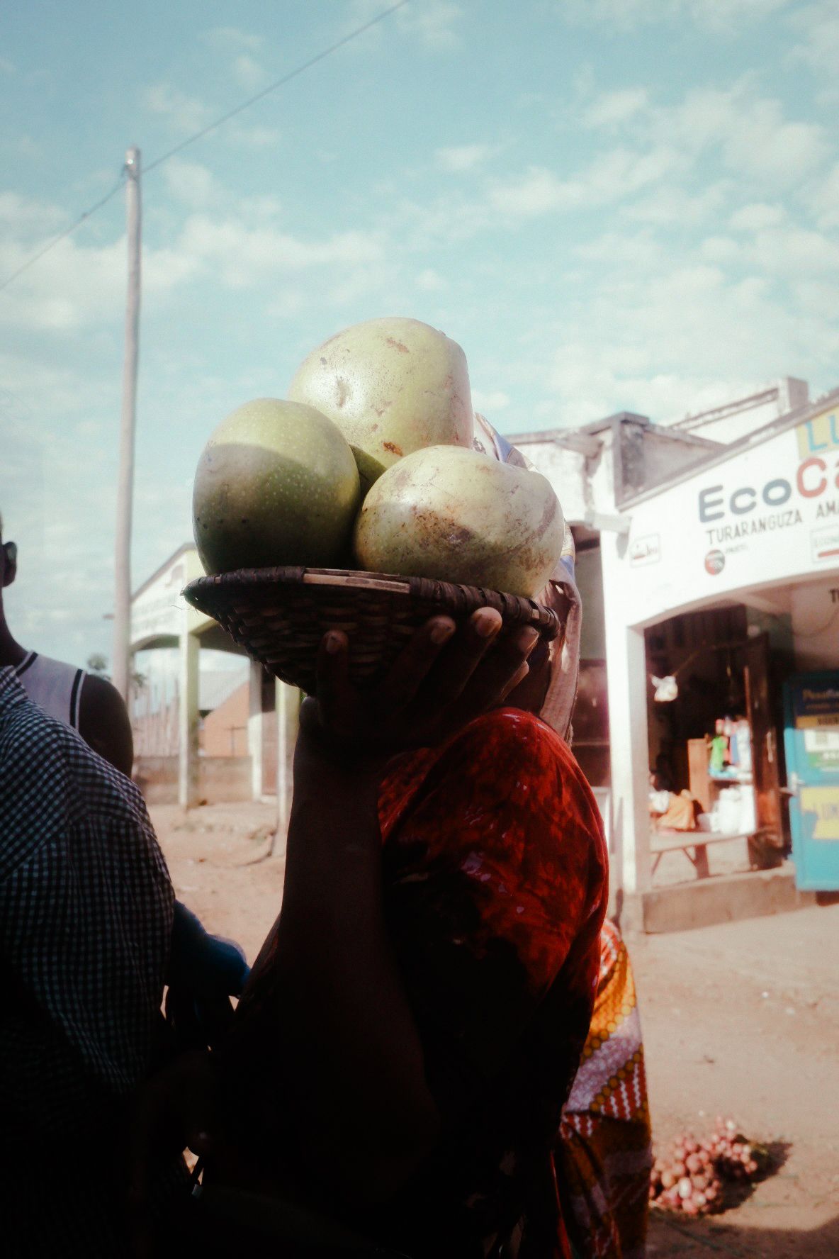 People carrying large water containers on their heads in a dusty street setting.