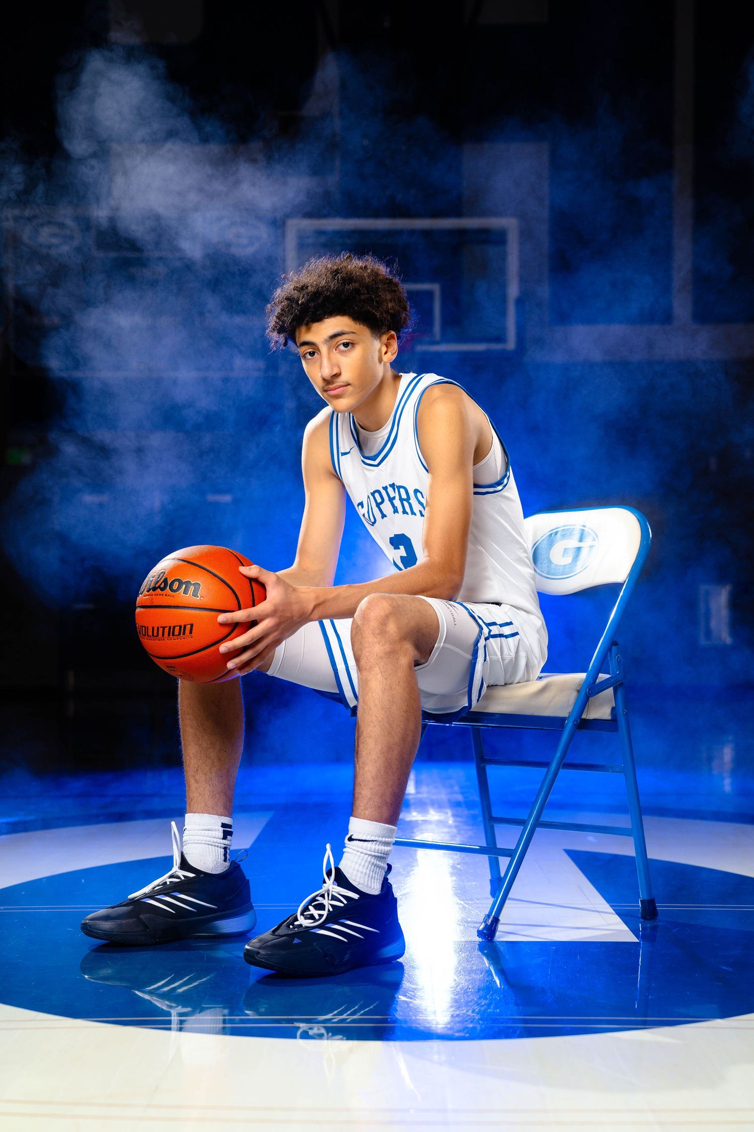 Basketball player in white uniform sits on chair against dramatic blue lighting and smoke effects.