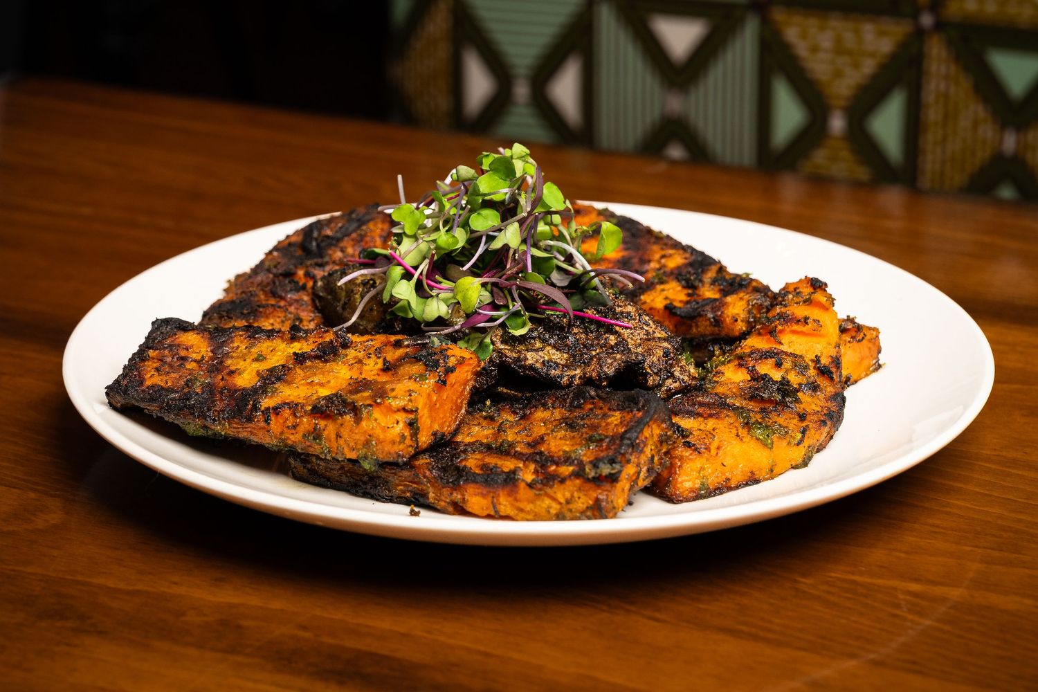 Grilled spiced flatbread topped with fresh microgreens served on a white plate on wooden table.