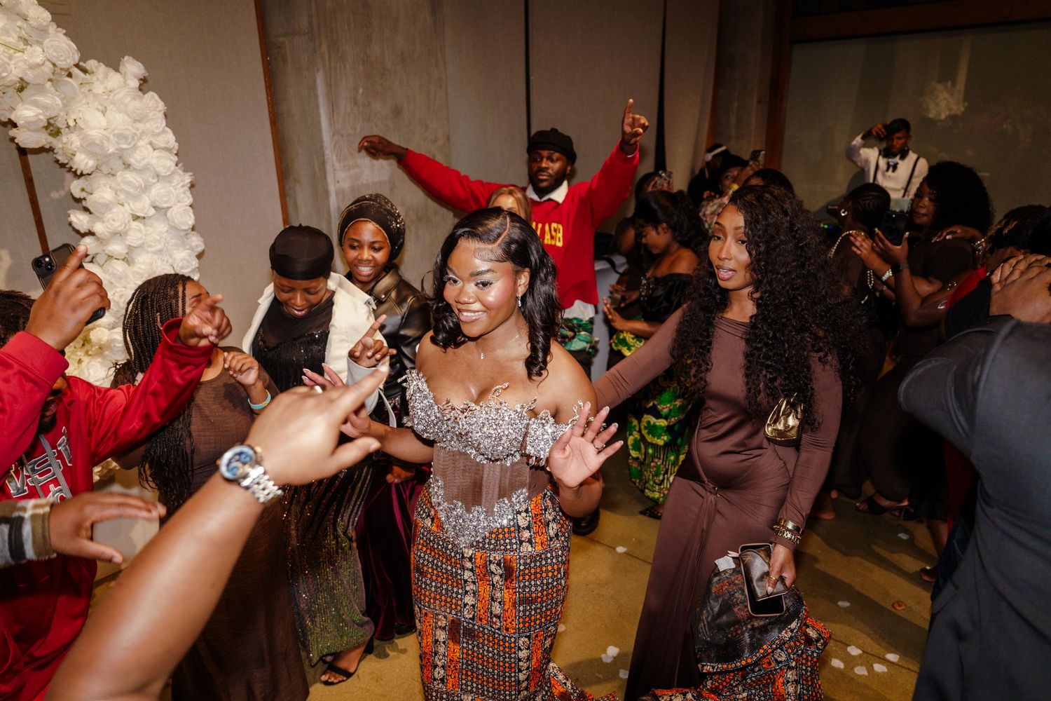 Group of people dancing and celebrating at a festive party event, wearing elegant outfits in a decorated venue.