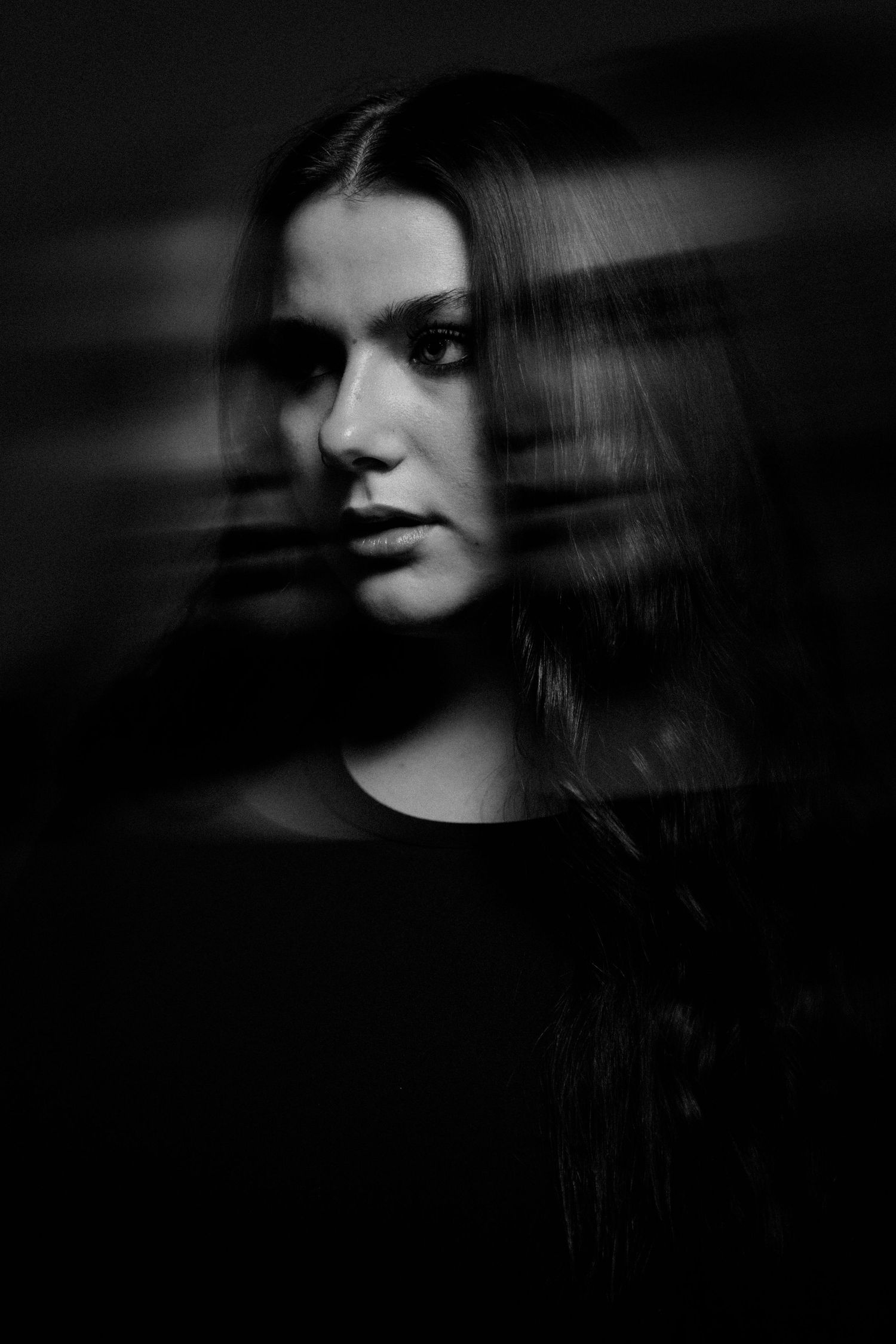 Black and white artistic portrait of a young woman with long dark hair and a mysterious, moody expression.