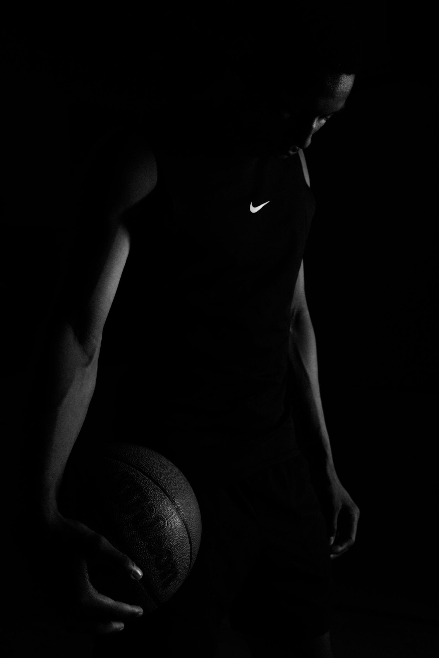 Silhouetted athlete holds basketball in dramatic spotlight.