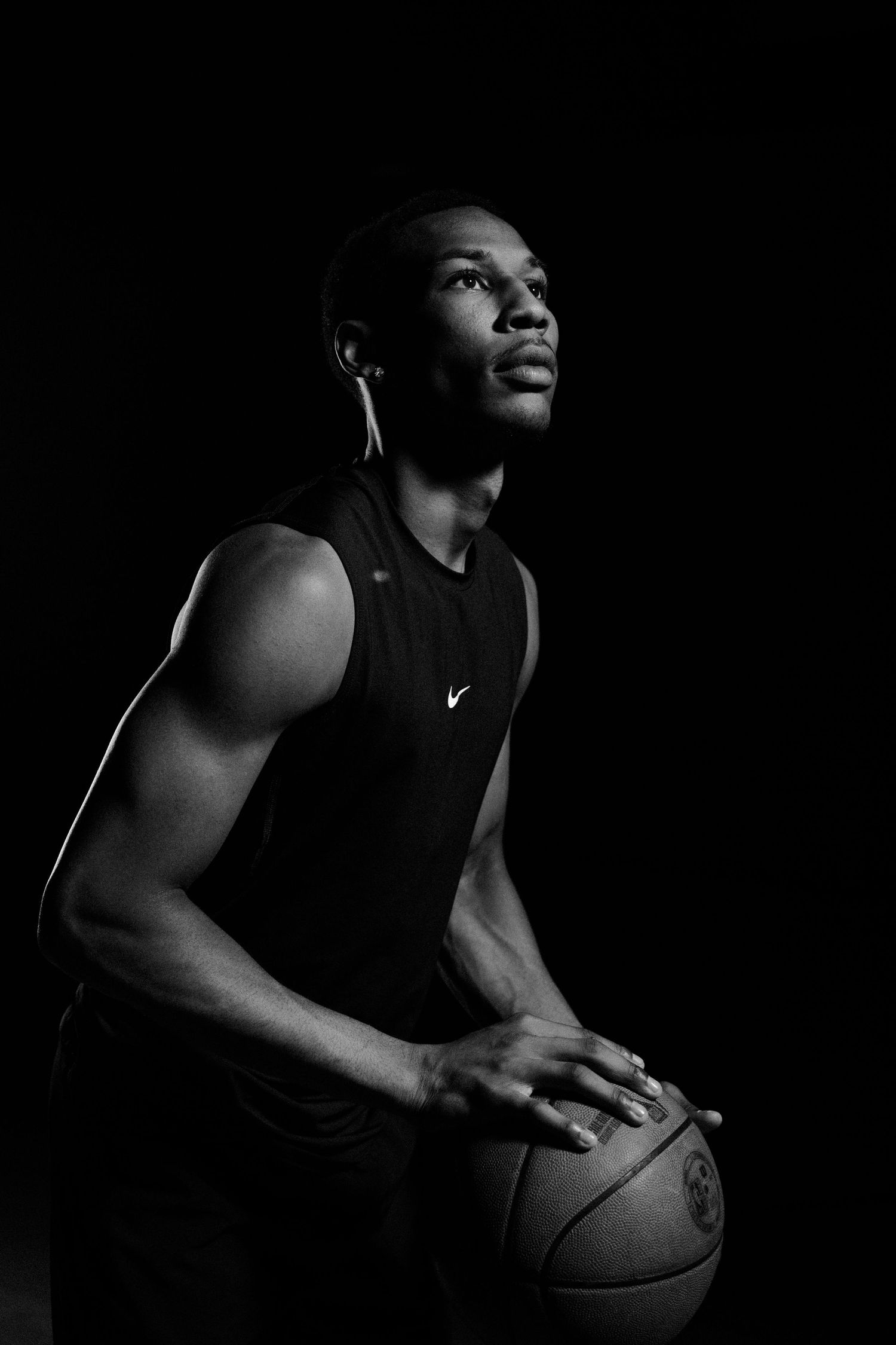 Dramatic black and white series of basketball player holding ball in Nike tank top with moody lighting and shadows.