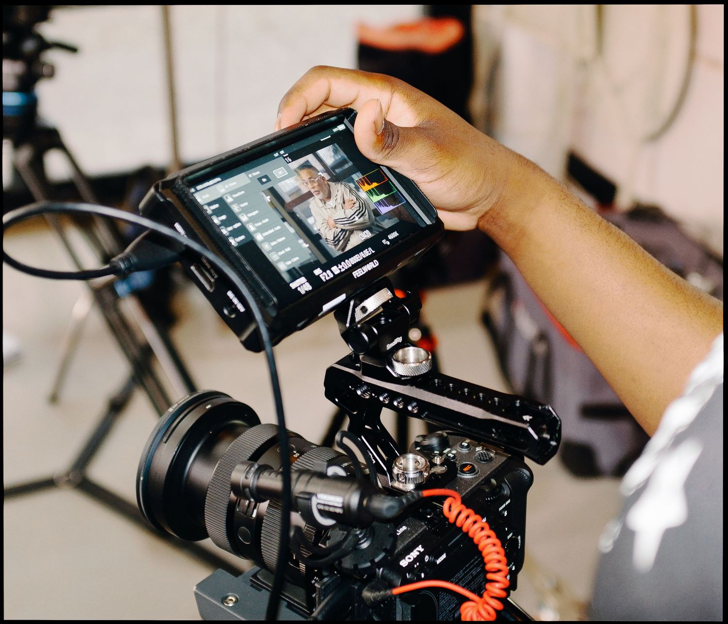 A videographer adjusts settings on a monitor mounted to a professional cinema camera on a film set.