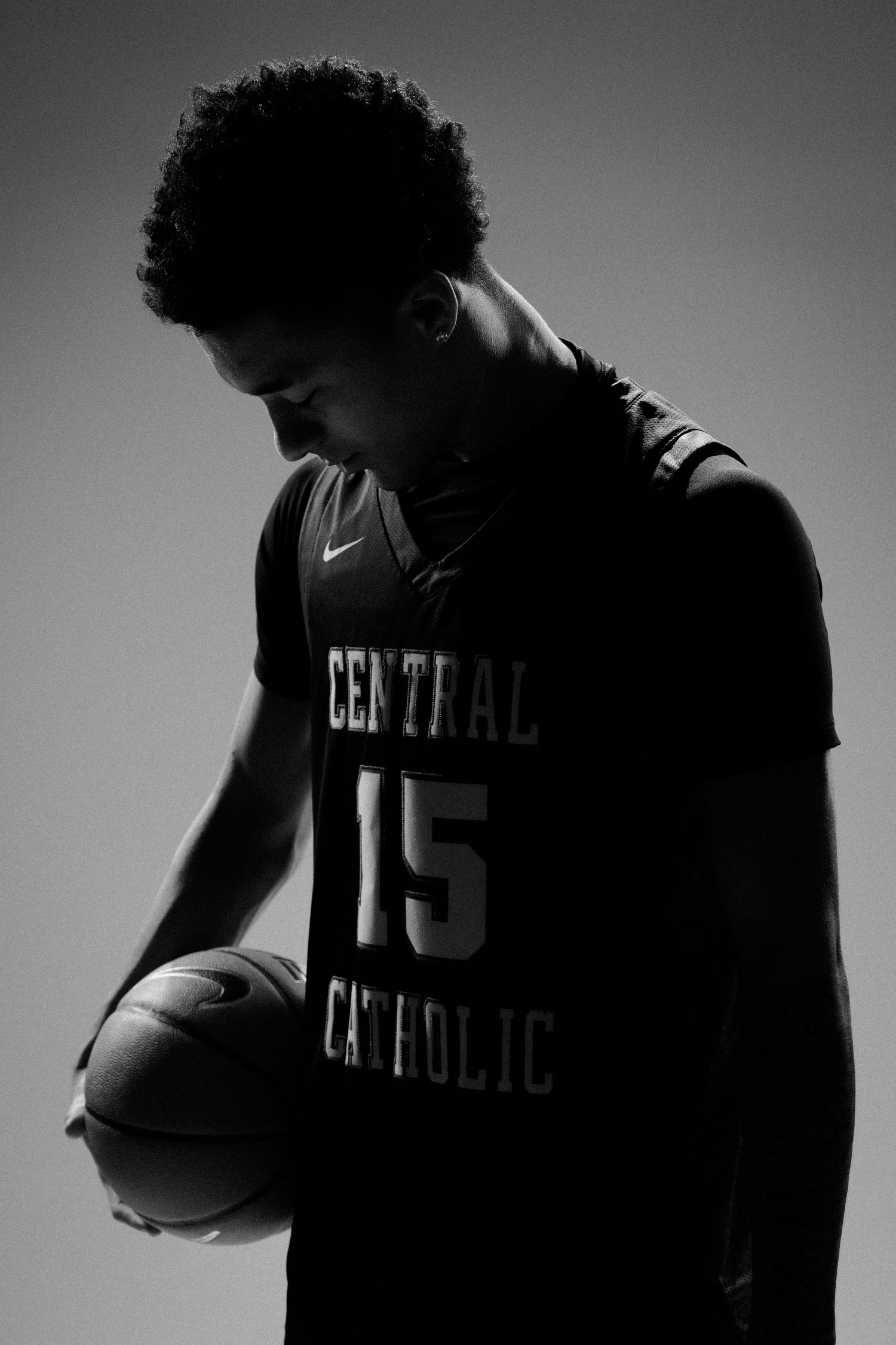 Dramatic side-lit silhouettes of basketball player in Central Catholic uniform.