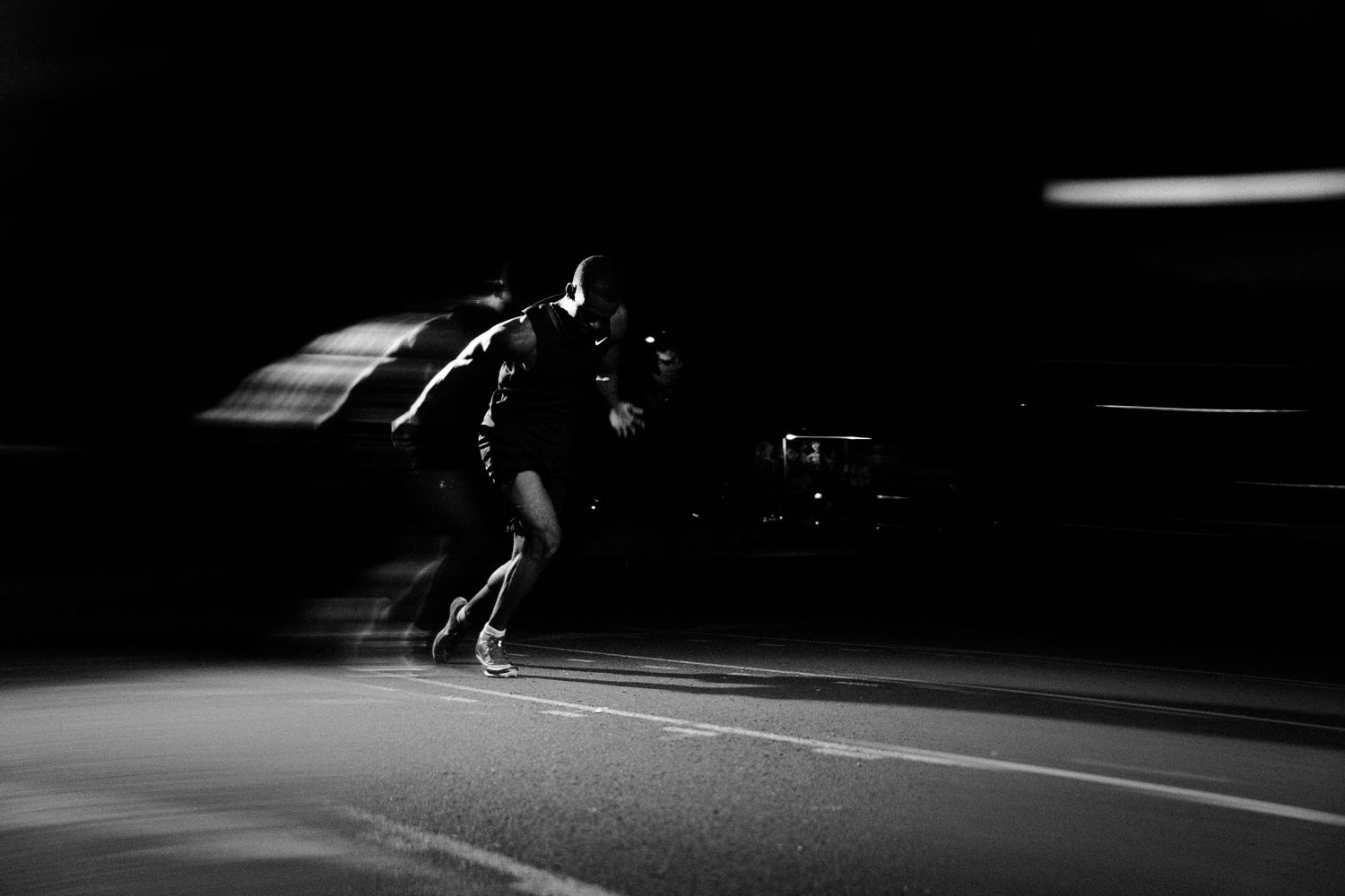 Black and white photo of a speed skater in motion on a dark road at night, captured with motion blur.