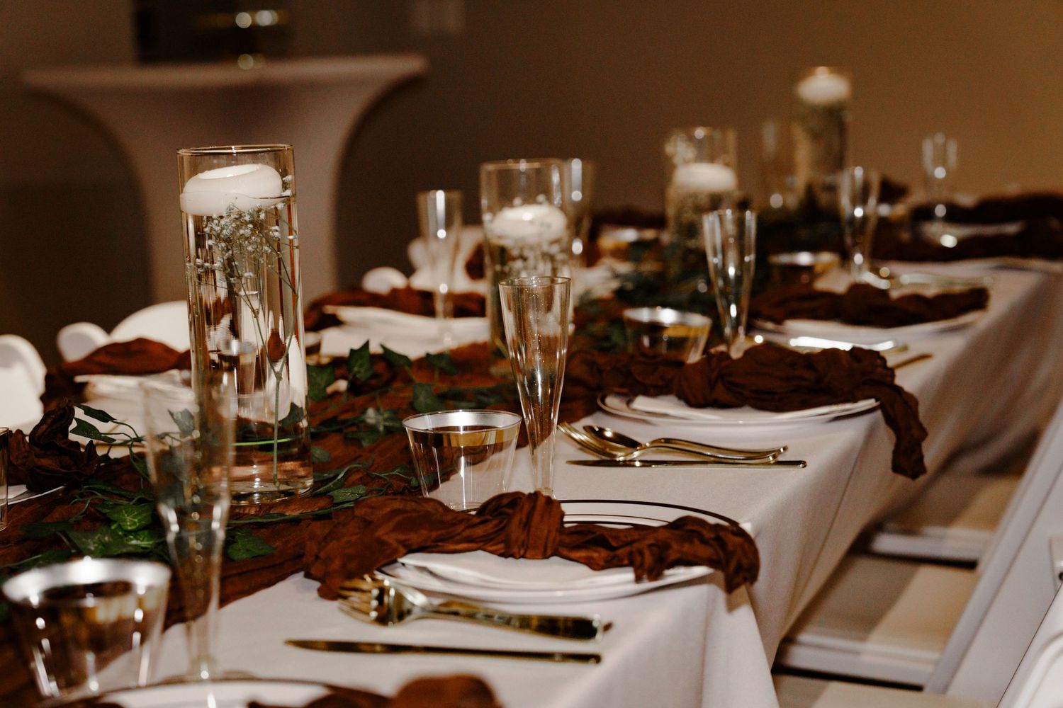Elegant banquet table set with gold cutlery, champagne flutes, and dark floral runner on white linen.