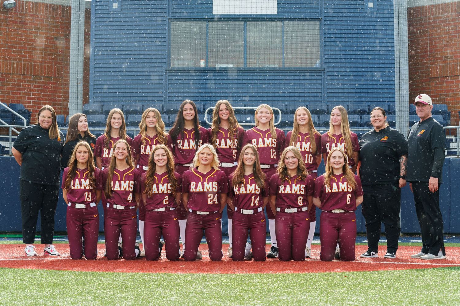 A sports team in maroon uniforms poses together on a field for a group photo.