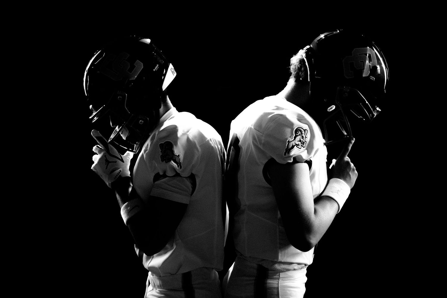 Two American football players in white uniforms and helmets posed back-to-back in a dramatic black and white photo.