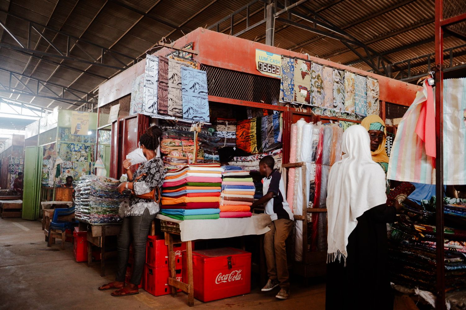 Indoor marketplace corridor with red poles and various retail stalls visible.