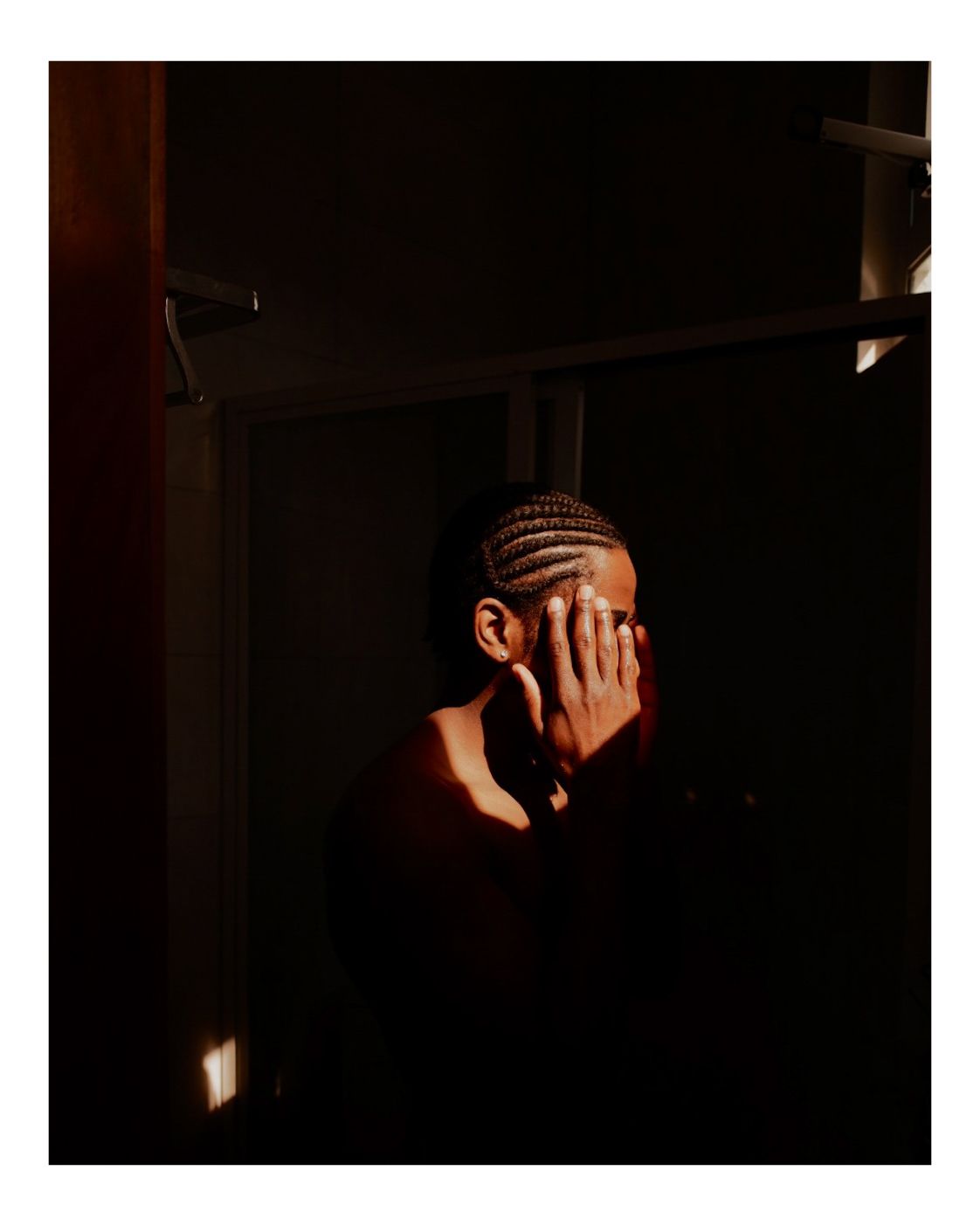 Atmospheric black and white portrait with hands covering face in dim light.