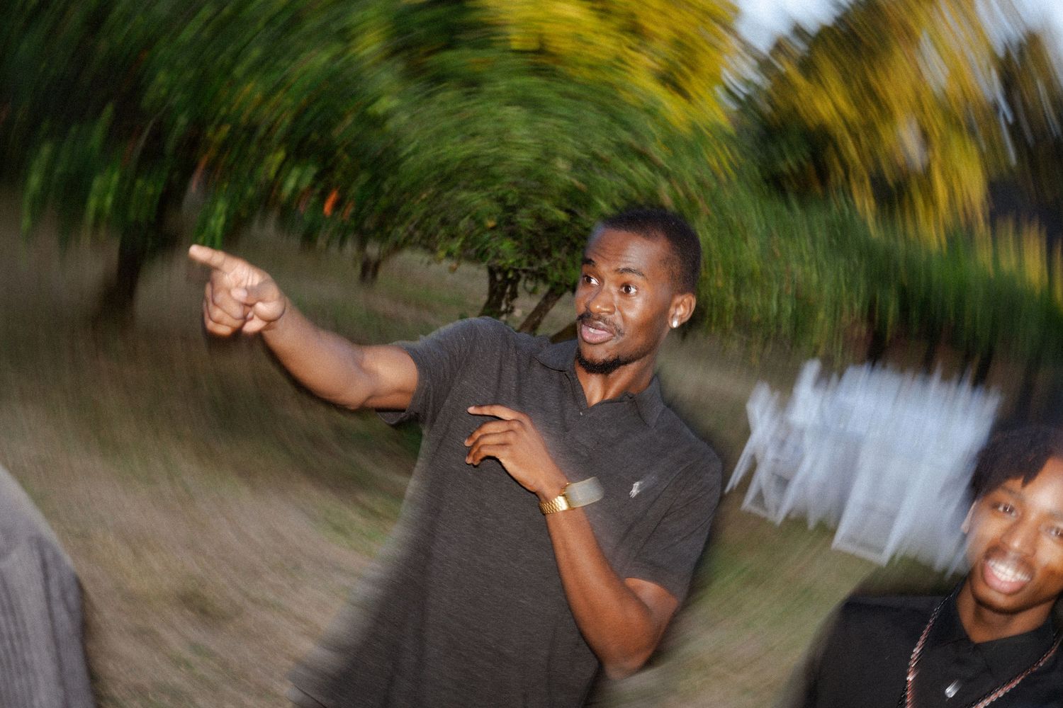Man in gray shirt pointing outdoors with motion blur background of green trees.