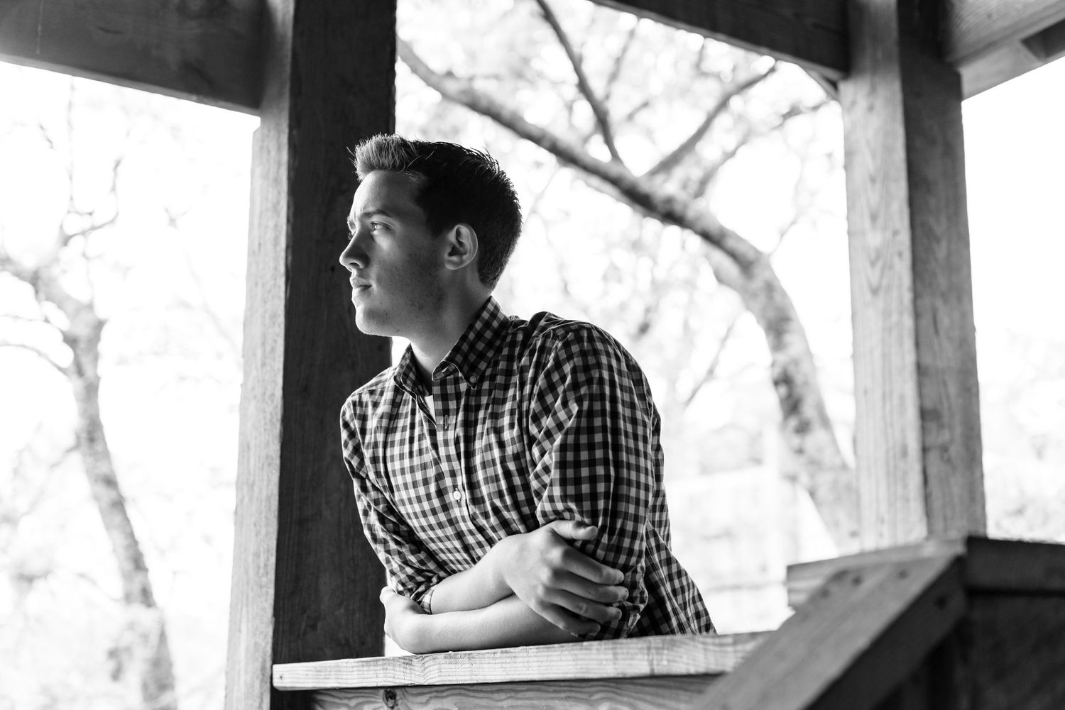 Black and white portrait of person looking out from covered porch.