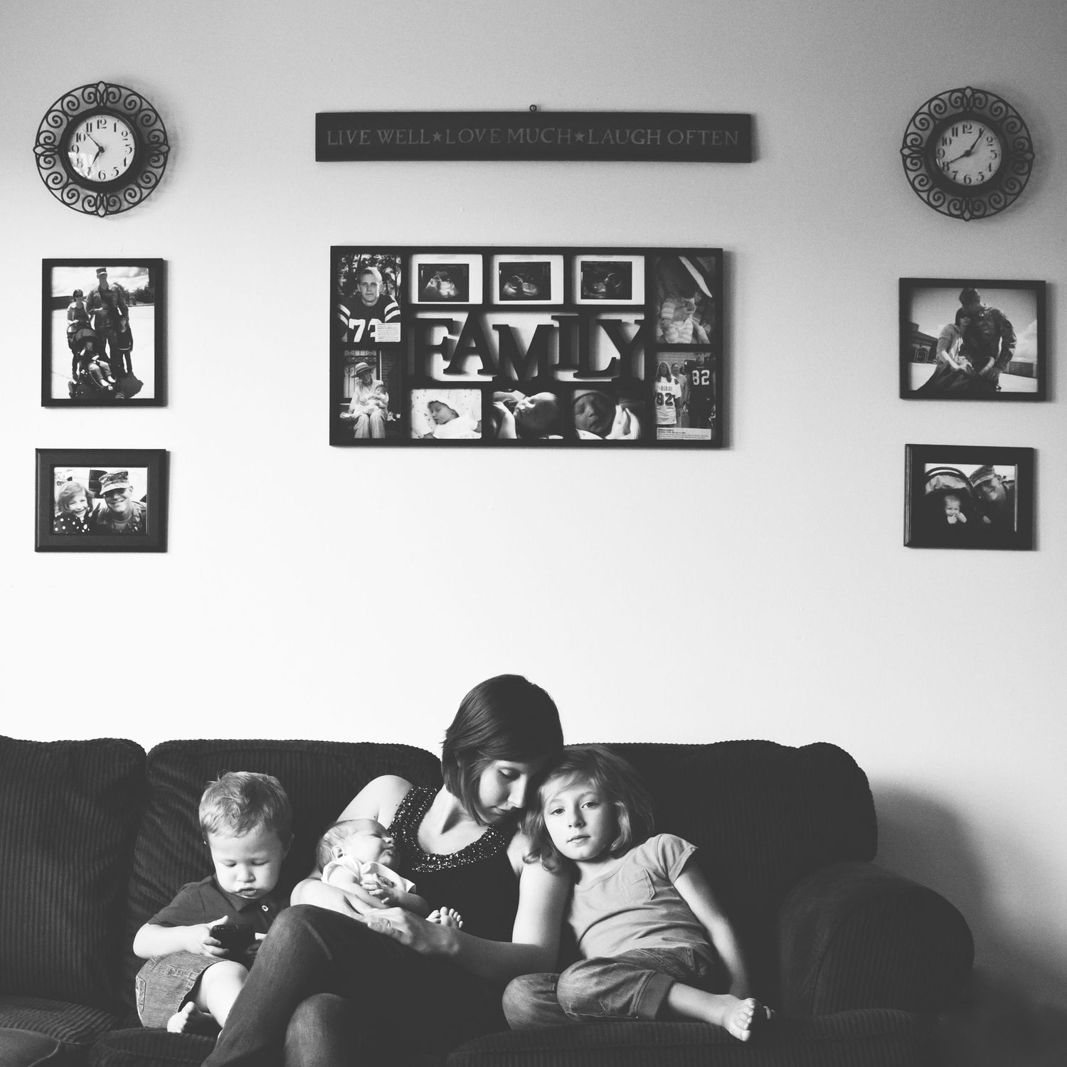Black and white photo of family relaxing on couch beneath wall of framed photos.